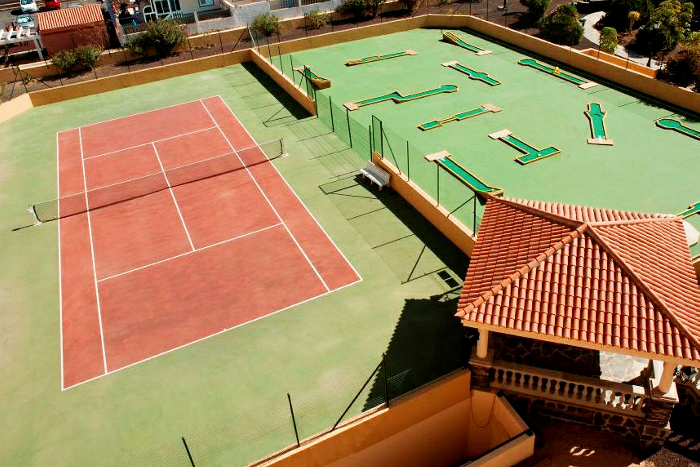 Tennisbana och minigolfområde bredvid en byggnad med rött tak. (AI-genererad text)