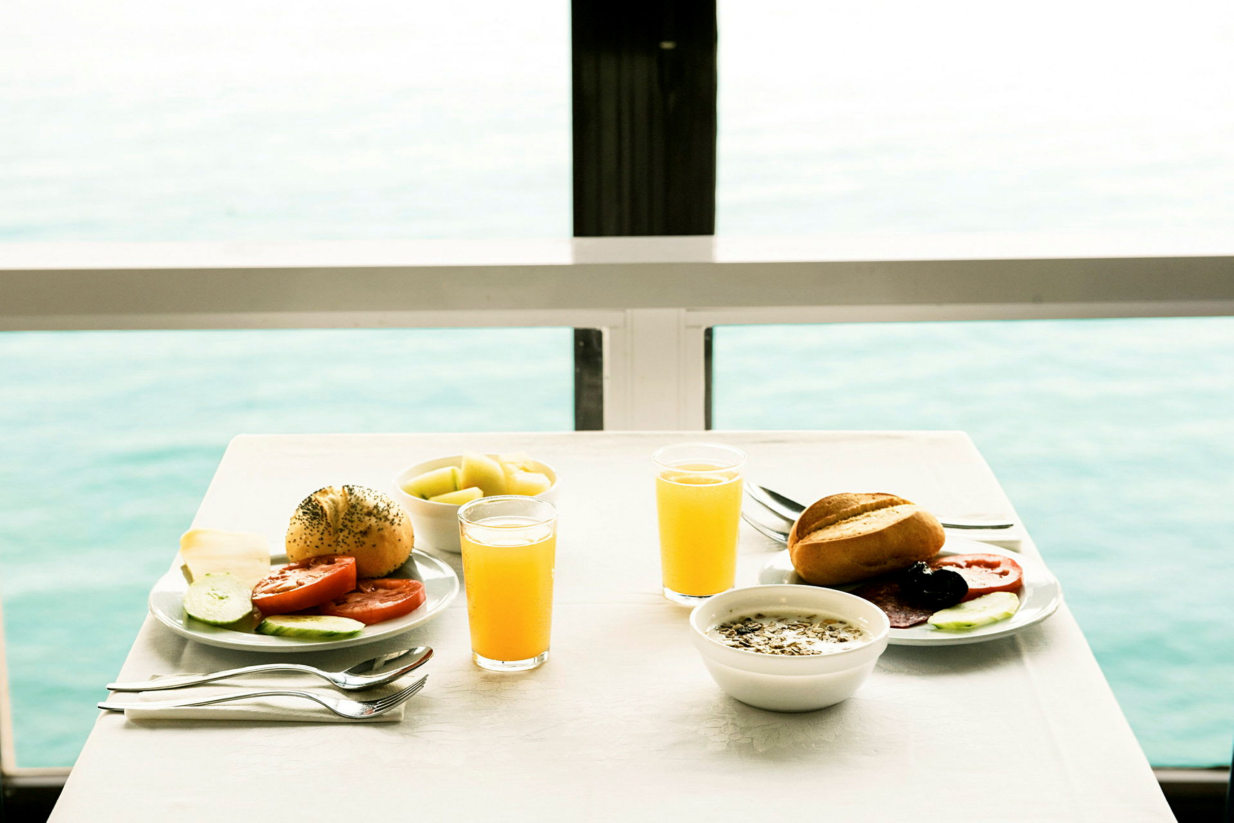 Två tallrikar med frukostmat, juiceglas, och en havsutsikt. (AI-genererad text)