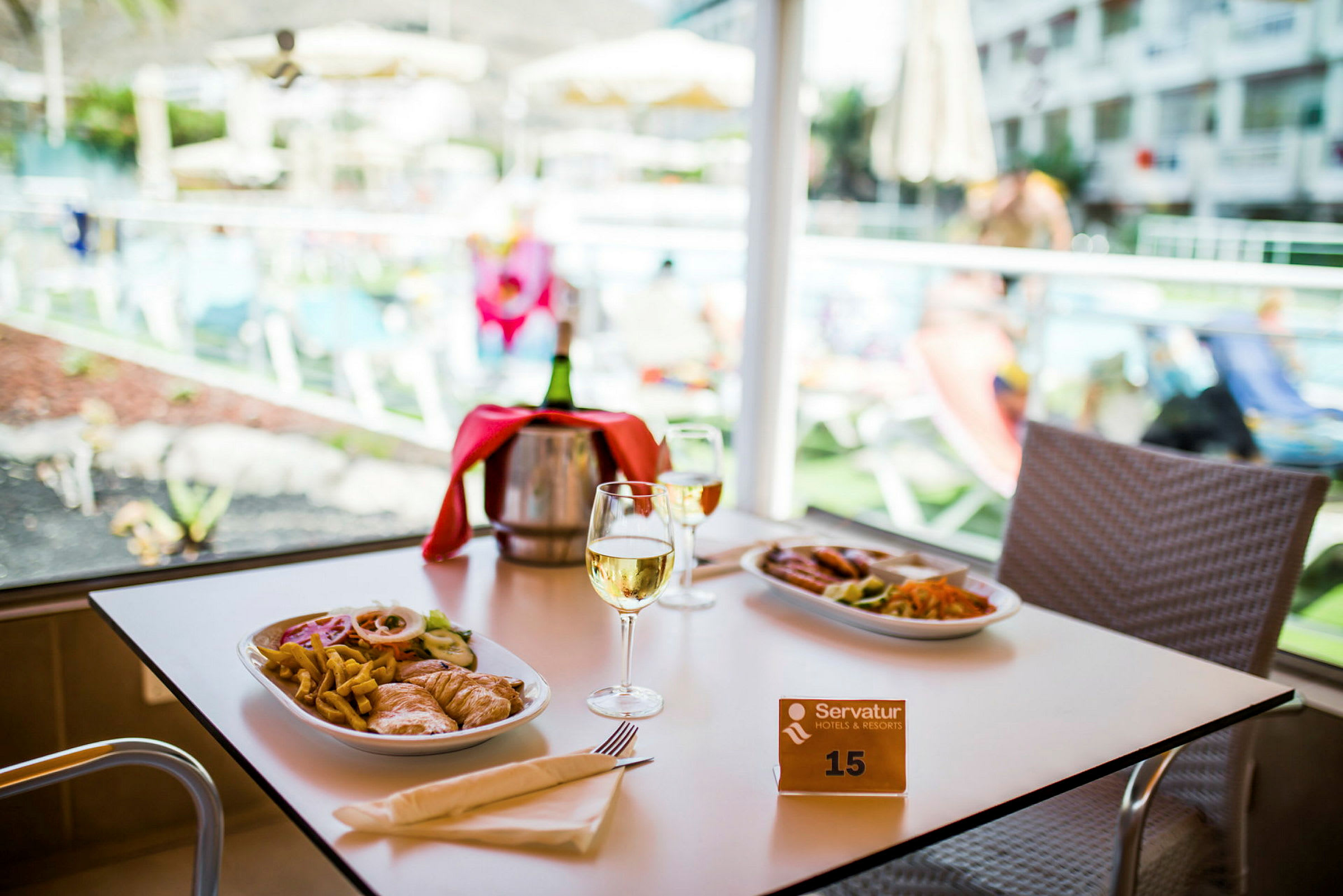 Ett bord med två tallrikar med mat och två glas vin framför en utsikt mot en pool. (AI-genererad text)