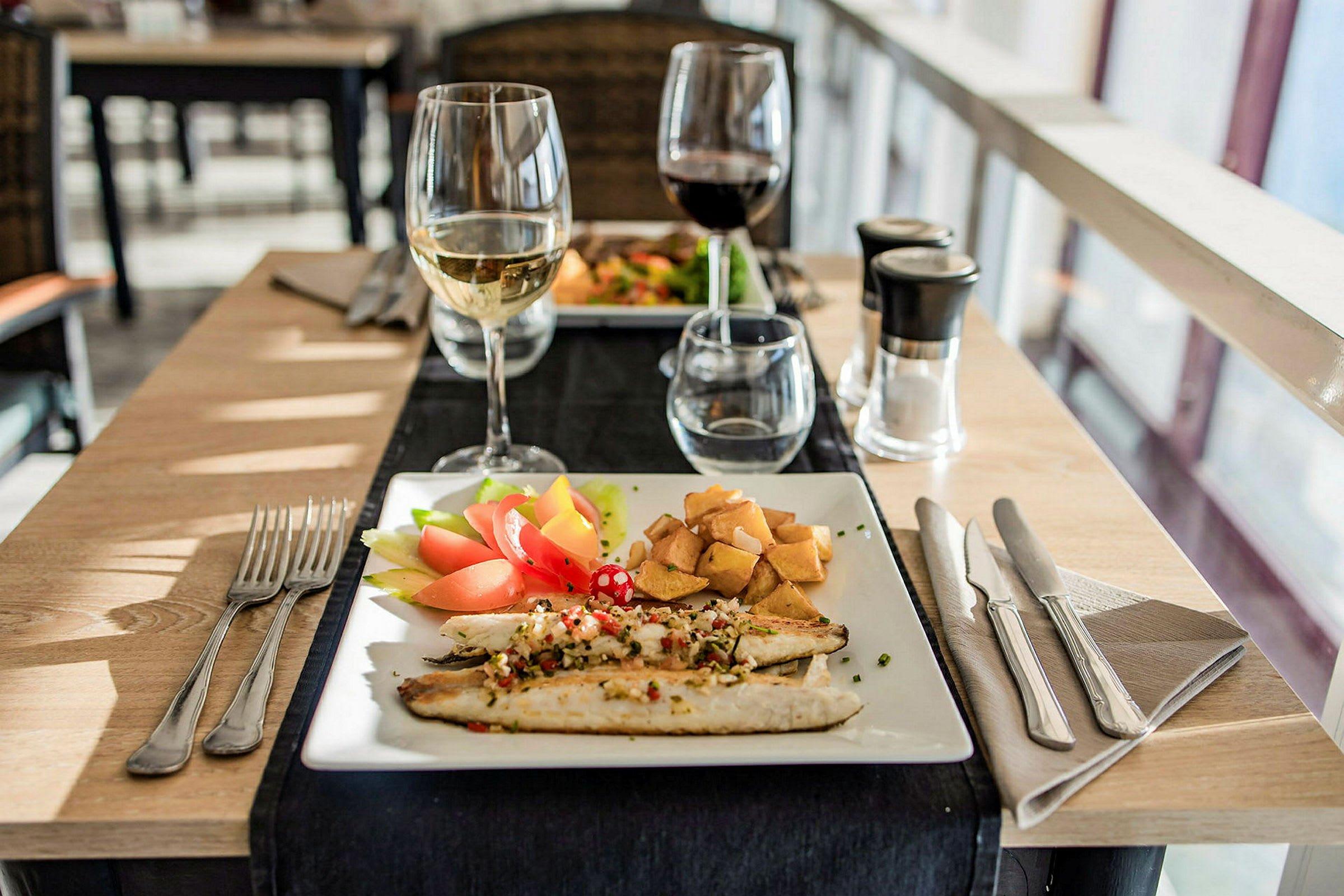 En tallrik med fisk, grönsaker och potatis, samt ett glas vitt vin. (AI-genererad text)