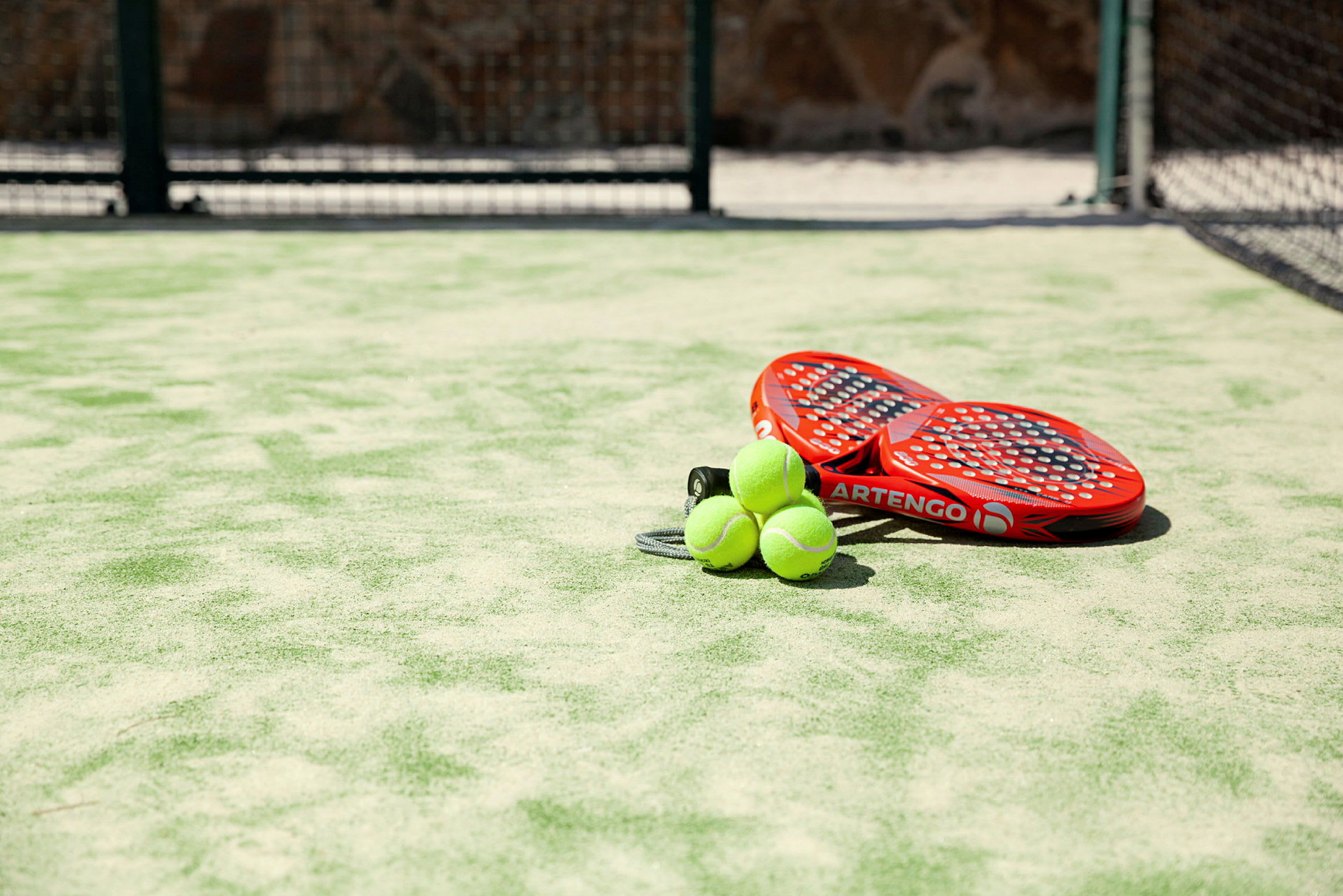 Två röda padelracketar och tre gröna bollar på en konstgräsplan. (AI-genererad text)