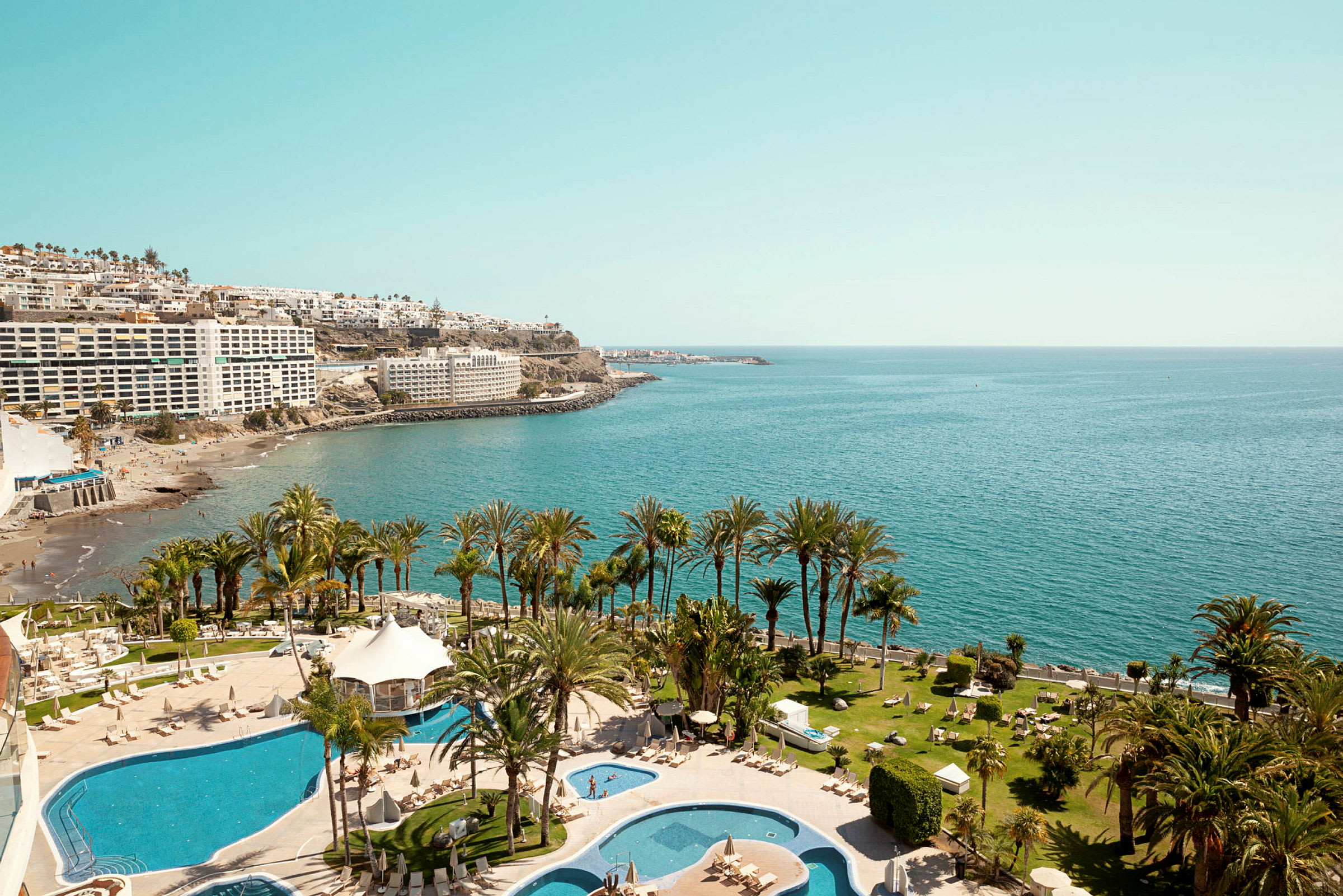 Vy över en resort med poolområden, palmer, strand och hav. (AI-genererad text)