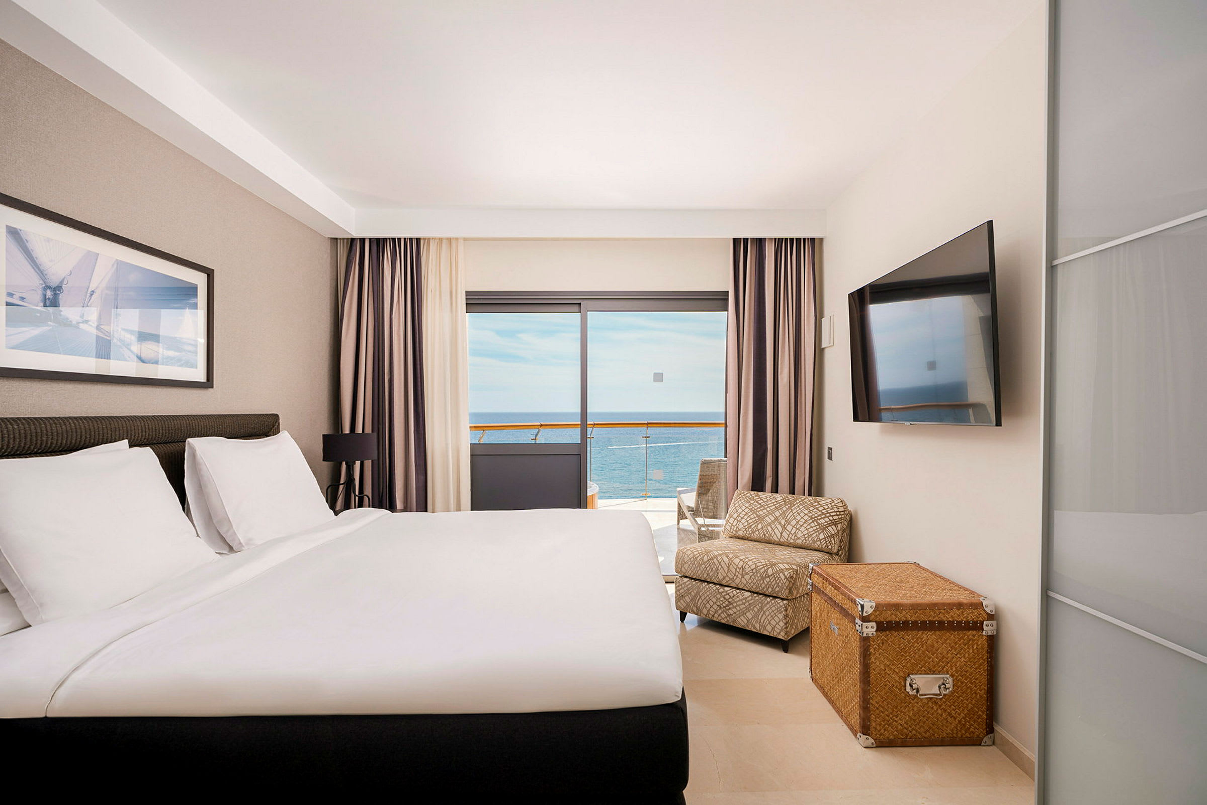 Hotellrum med säng, sittmöbler, vägg-TV och balkong med havsutsikt. (AI-genererad text)