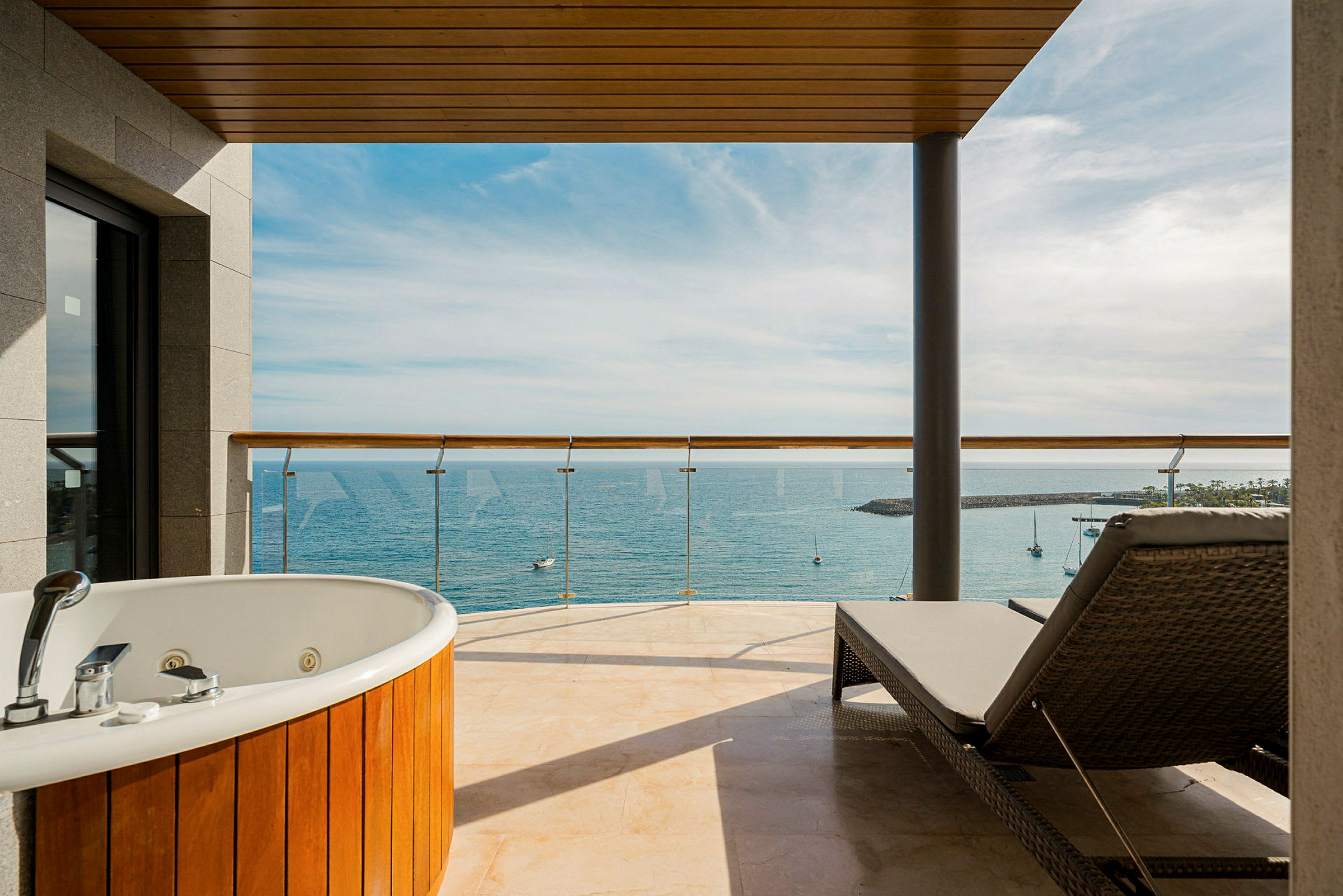 En hotellbalkong med jacuzzi och solstol, utsikt över hav och småbåtar. (AI-genererad text)