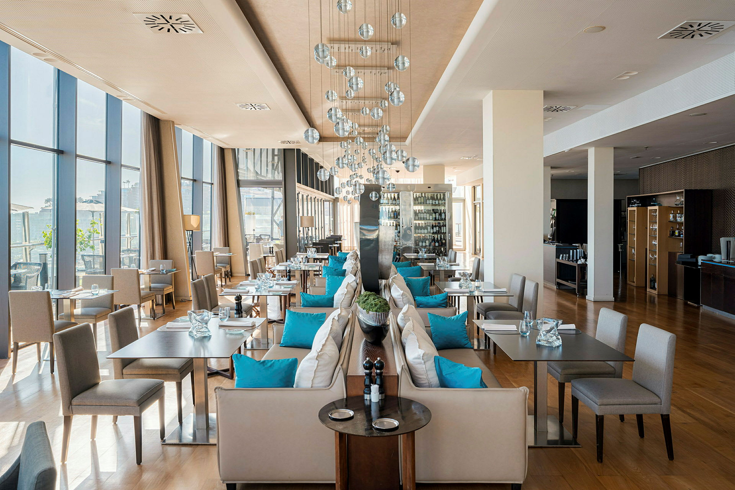 En stilren restaurang med stora fönster, bänkar dekorerade med blå kuddar och moderna lampor. (AI-genererad text)