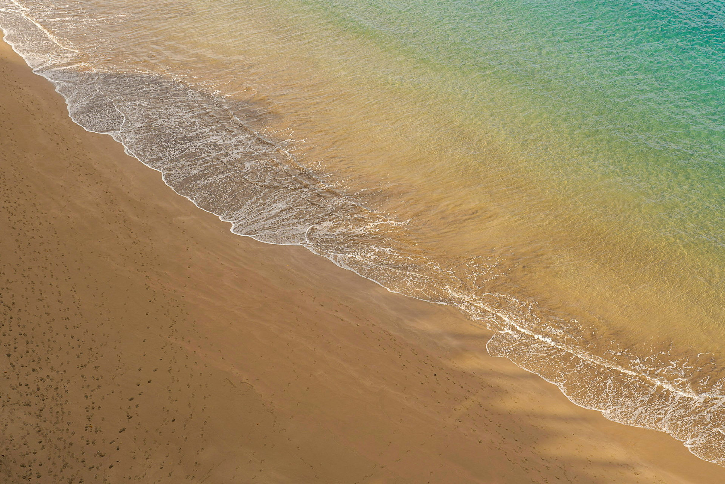 Bilden föreställer en sandstrand med vågor från havet som når kanten. (AI-genererad text)