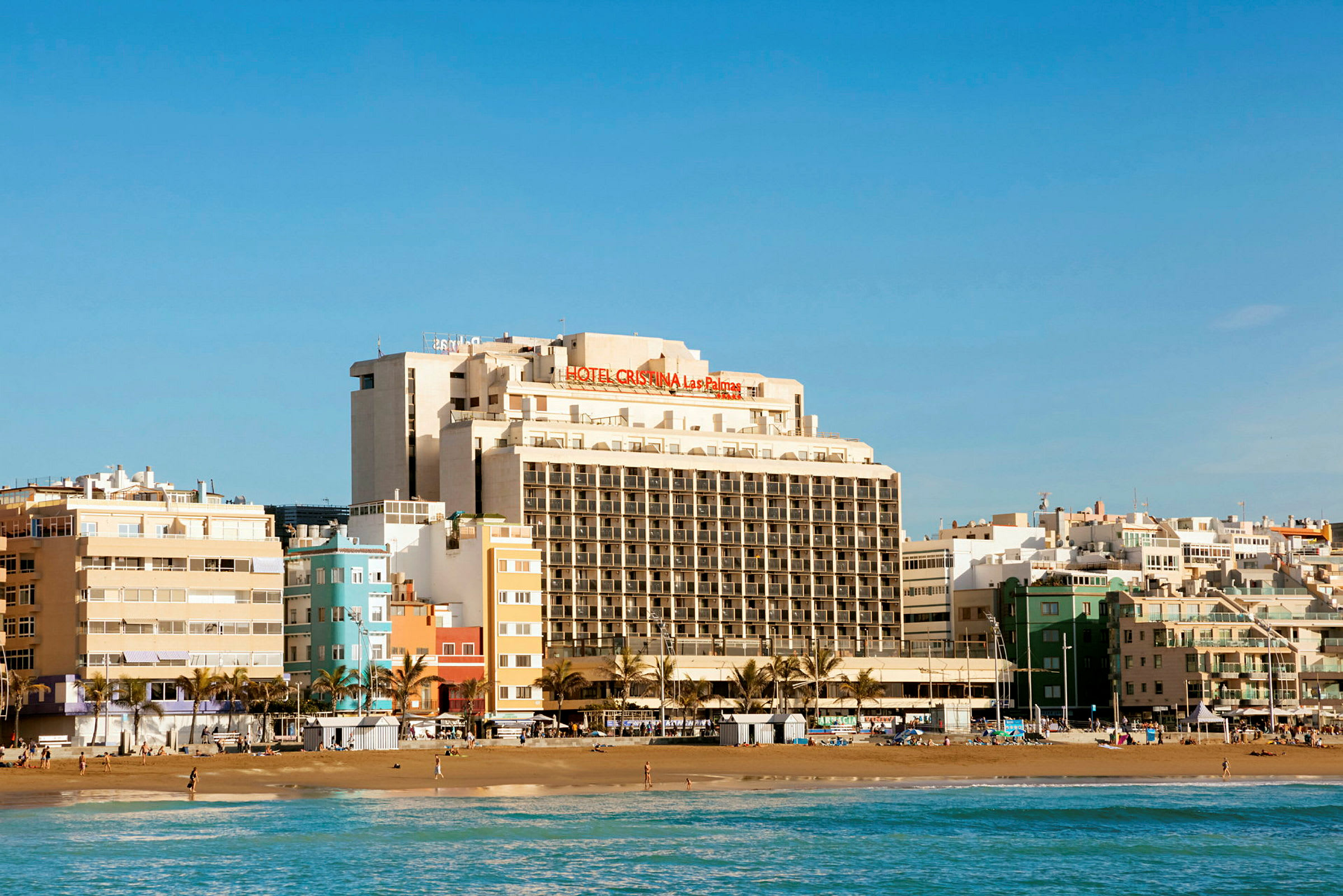 Vy över en strand med en stor hotellbyggnad i bakgrunden. (AI-genererad text)