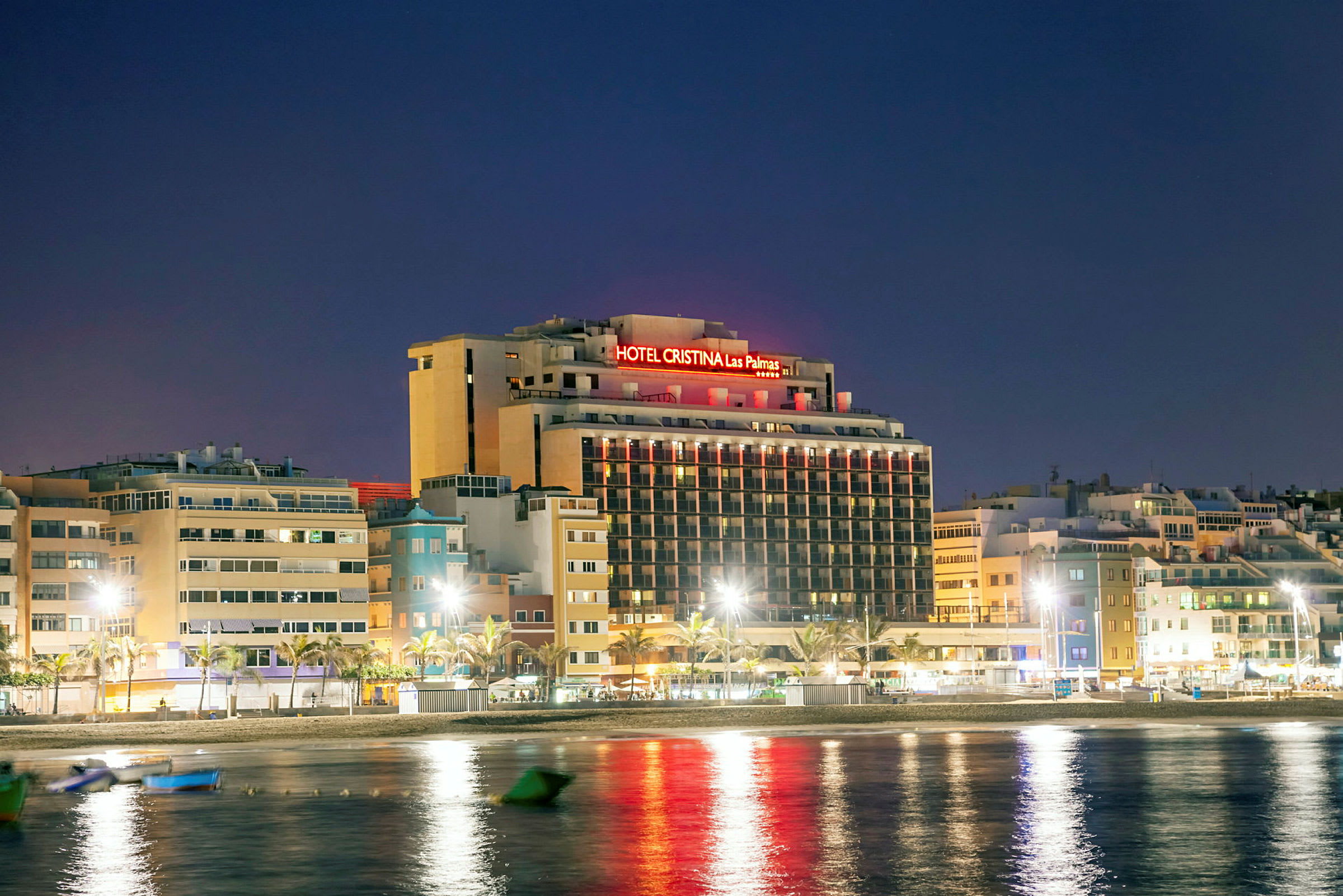 Bild av hotellbyggnad med neonljus i nattmiljö, belägen nära vatten. (AI-genererad text)