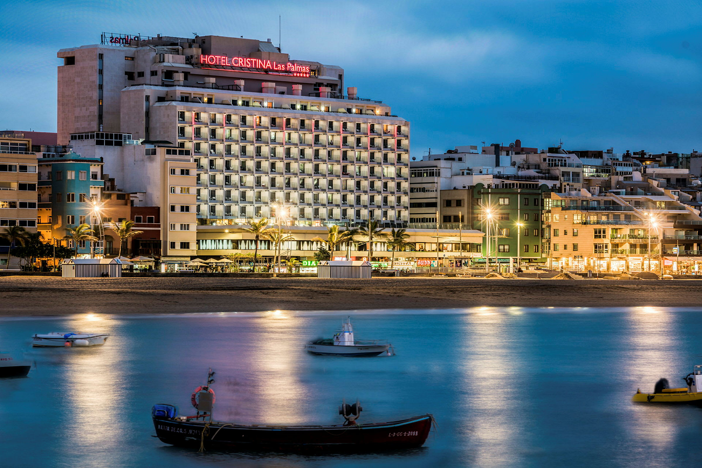 Hotellbyggnad nära strand, båtar på vatten i förgrunden. (AI-genererad text)