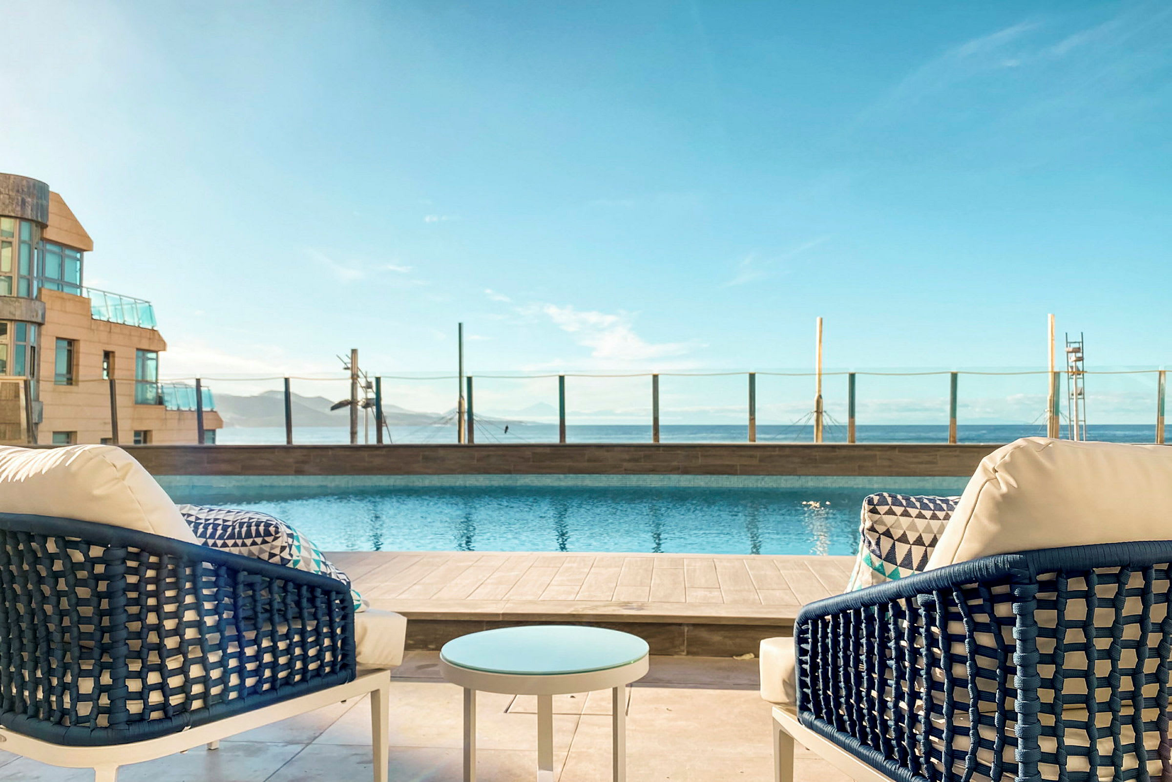 Två stolar och ett bord vid en pool med utsikt över havet. (AI-genererad text)