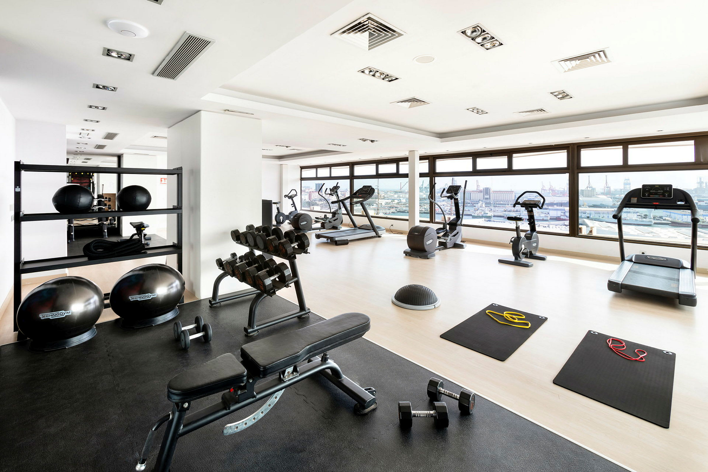 Bild av ett gym med konditionsmaskiner, bänkar, fria vikter och träningsmattor. (AI-genererad text)