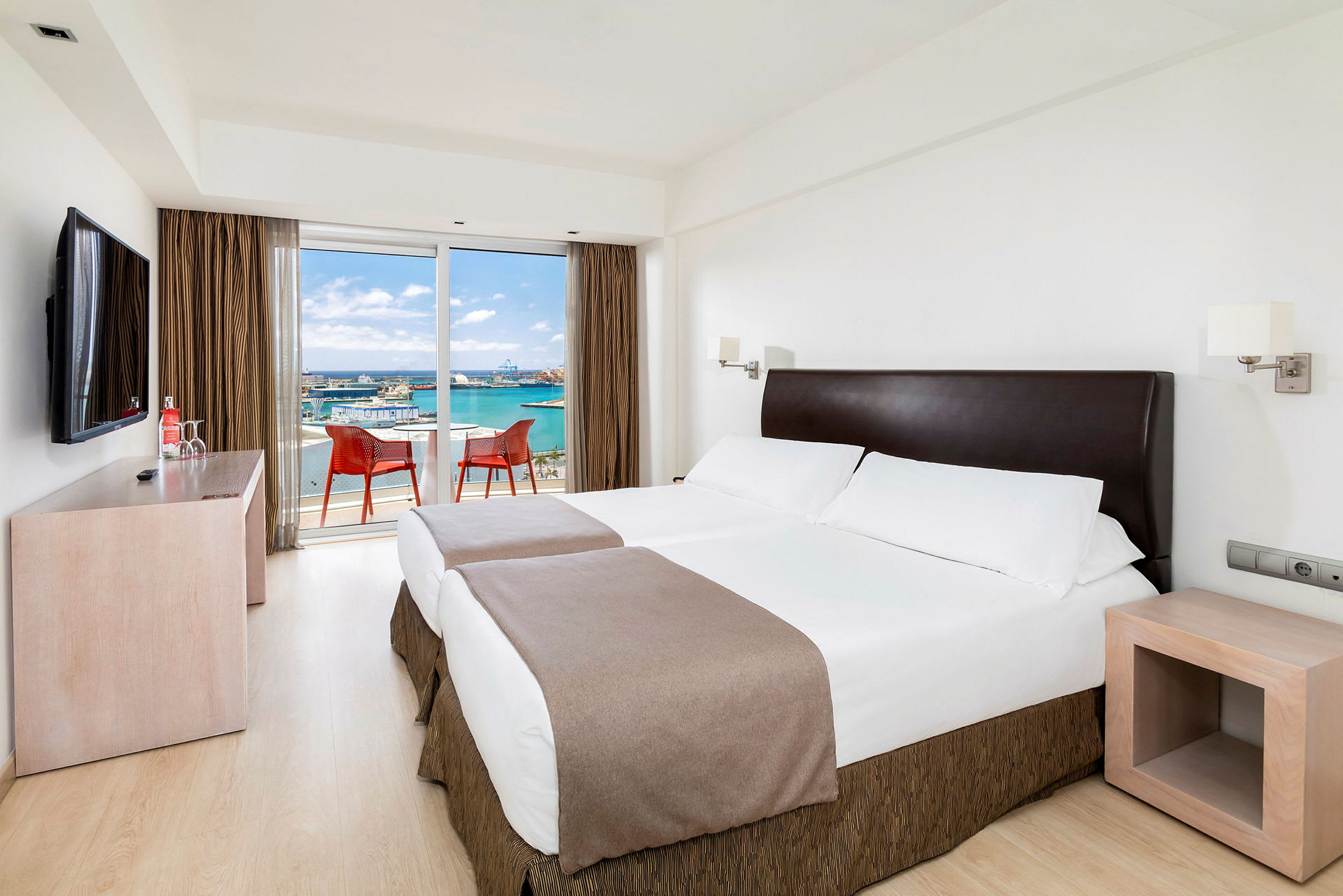 Ett hotellrum med två enkelsängar och en balkong med utsikt över havet. (AI-genererad text)
