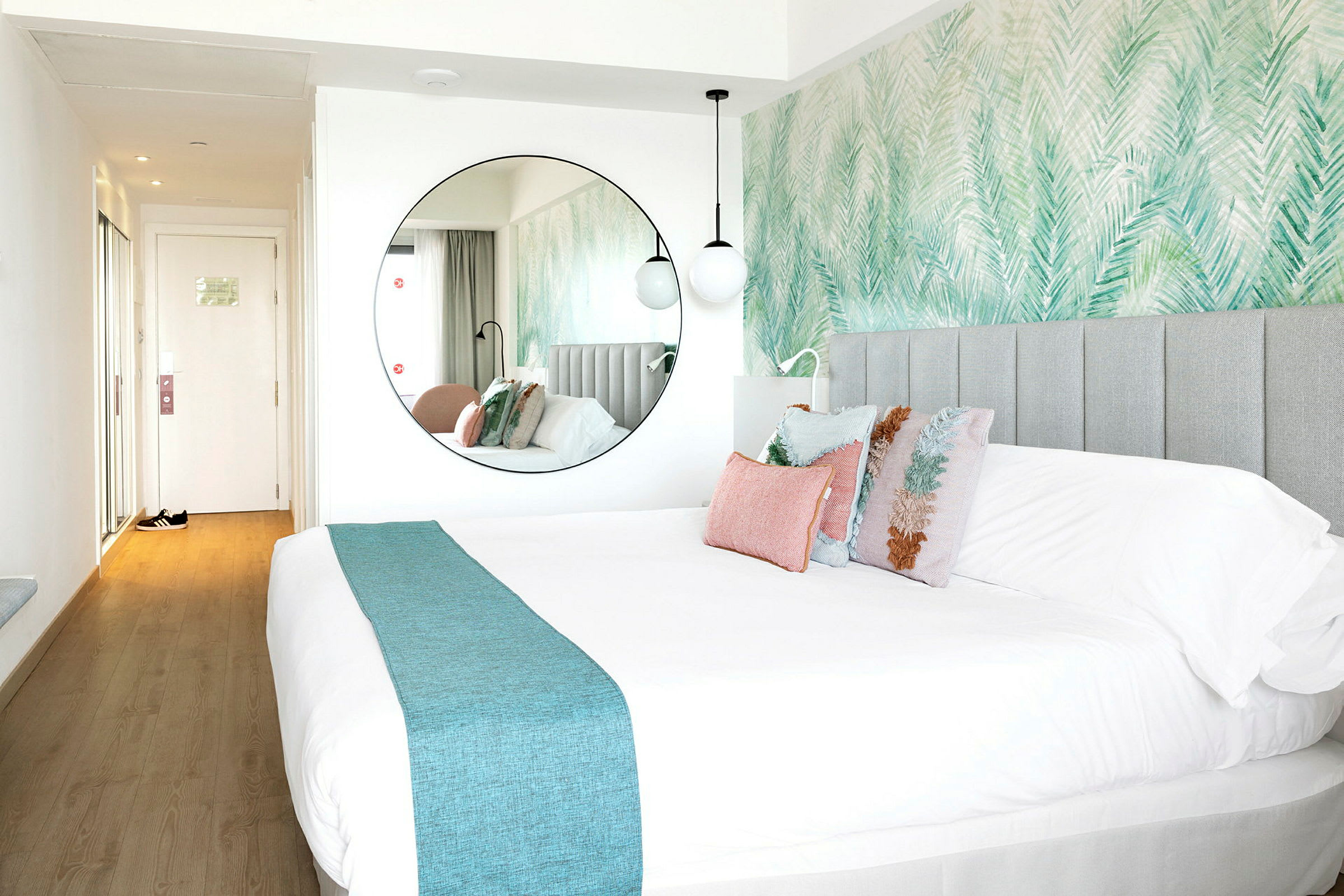 Ett hotellrum med en stor säng och dekorativa kuddar, samt en rund spegel på väggen. (AI-genererad text)