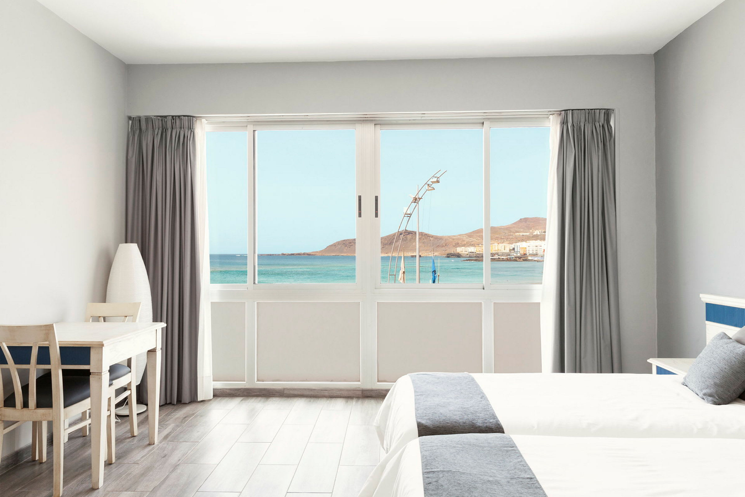 Ljust hotellrum med utsikt över havet genom en stor fönsterfront. (AI-genererad text)