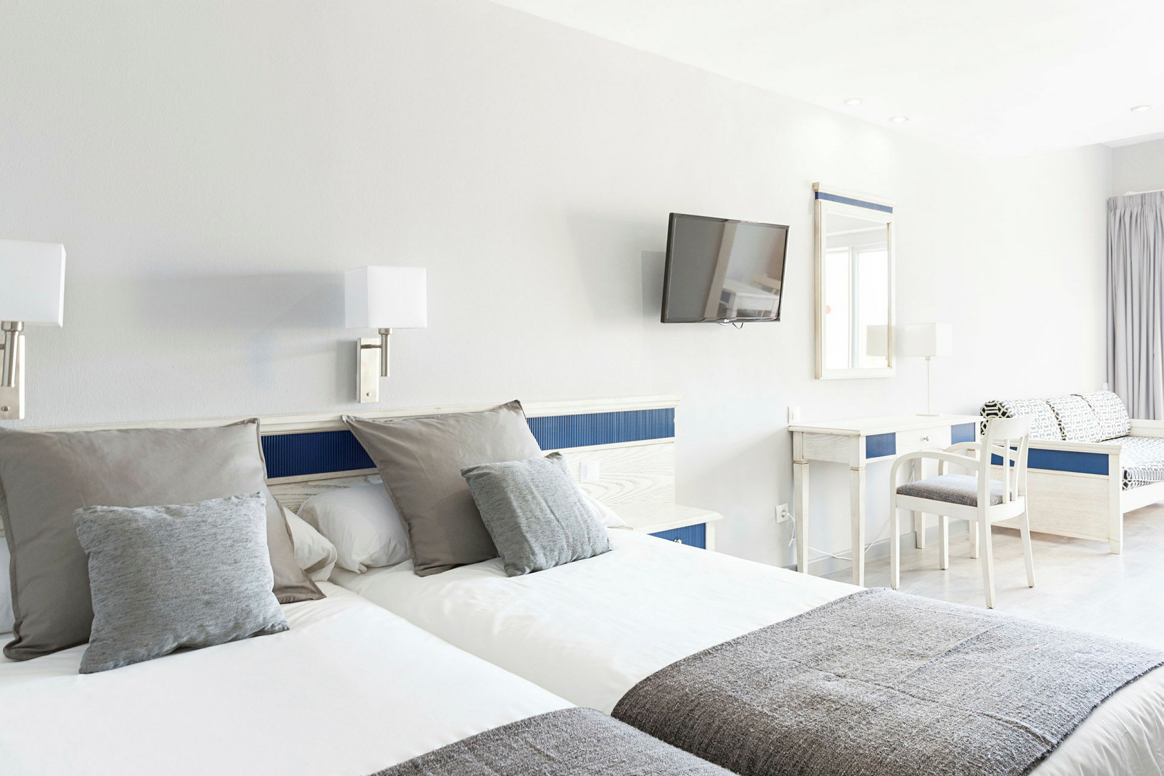 Hotellrum med två enkelsängar, skrivbord, stol och väggmonterad TV. (AI-genererad text)