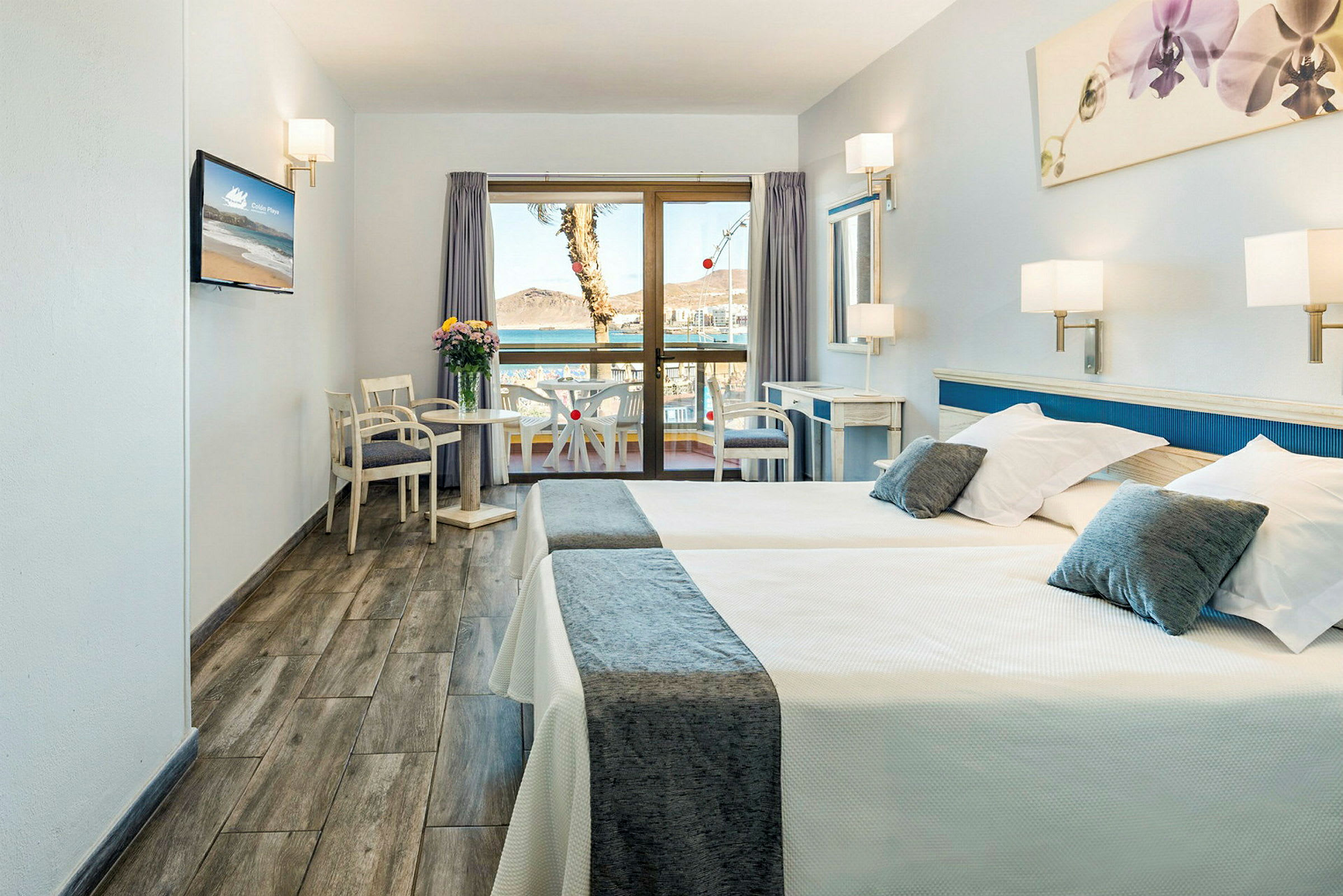 Hotellrum med två sängar, sittgrupp, skrivbord och balkong som vetter mot utsikten utomhus. (AI-genererad text)