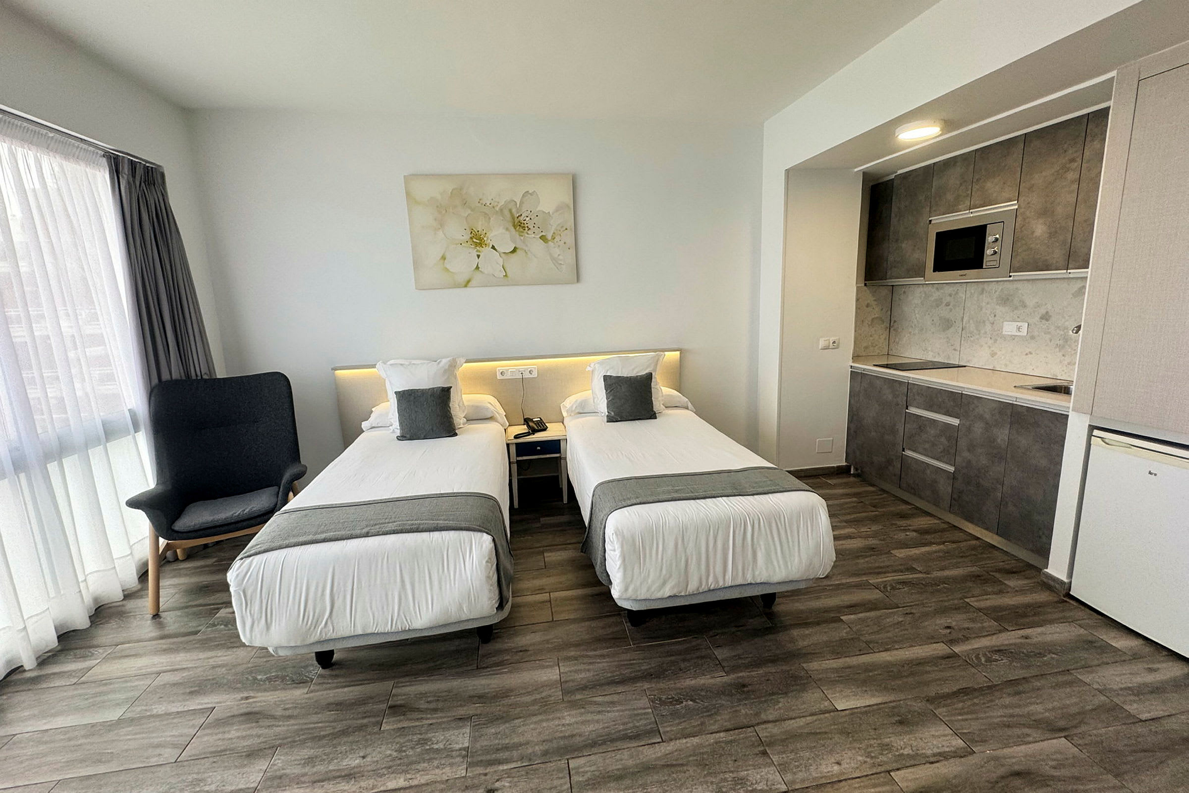 Ett hotellrum med två enkelsängar, en fåtölj och en kokvrå. (AI-genererad text)