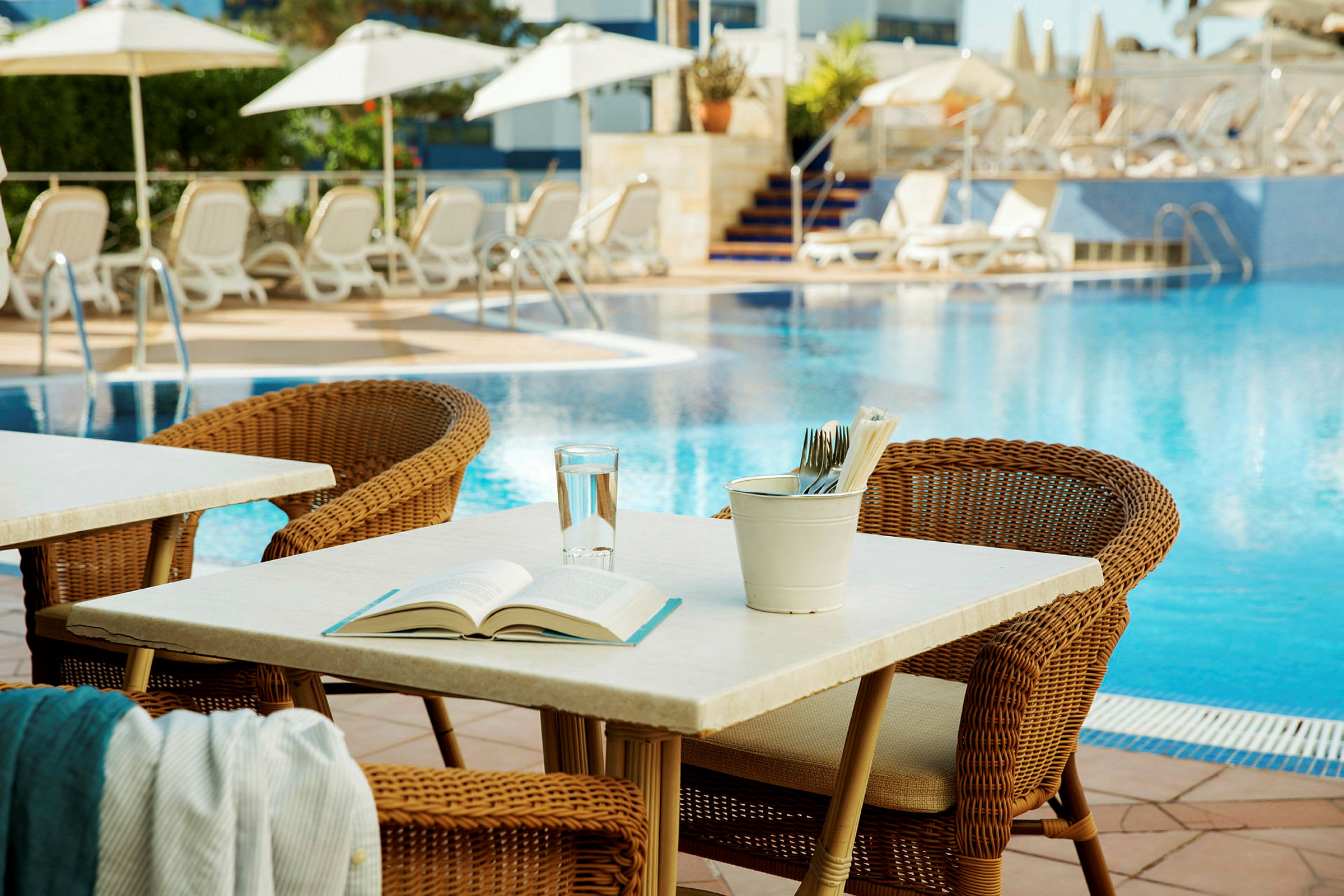 Utemöbler vid en pool med solstolar och parasoller i bakgrunden. (AI-genererad text)