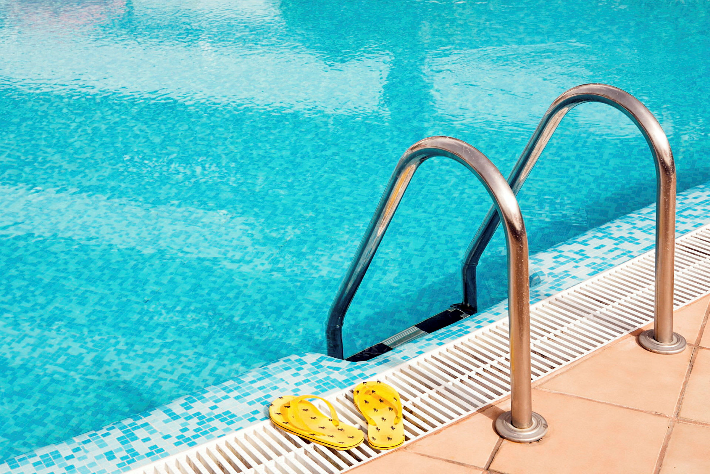 Bild på en pool med metallstegar, samt gula sandaler vid kanten. (AI-genererad text)