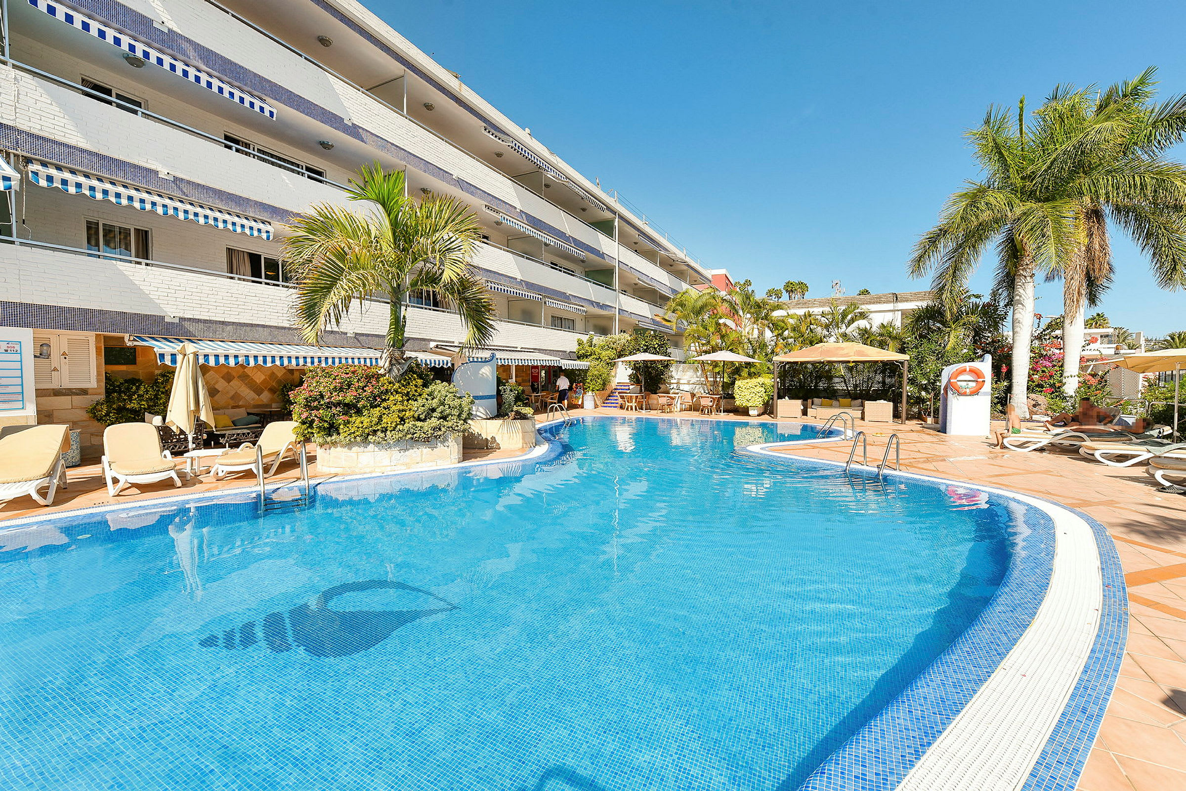 Utomhuspool vid hotell omgiven av solstolar och palmer. (AI-genererad text)
