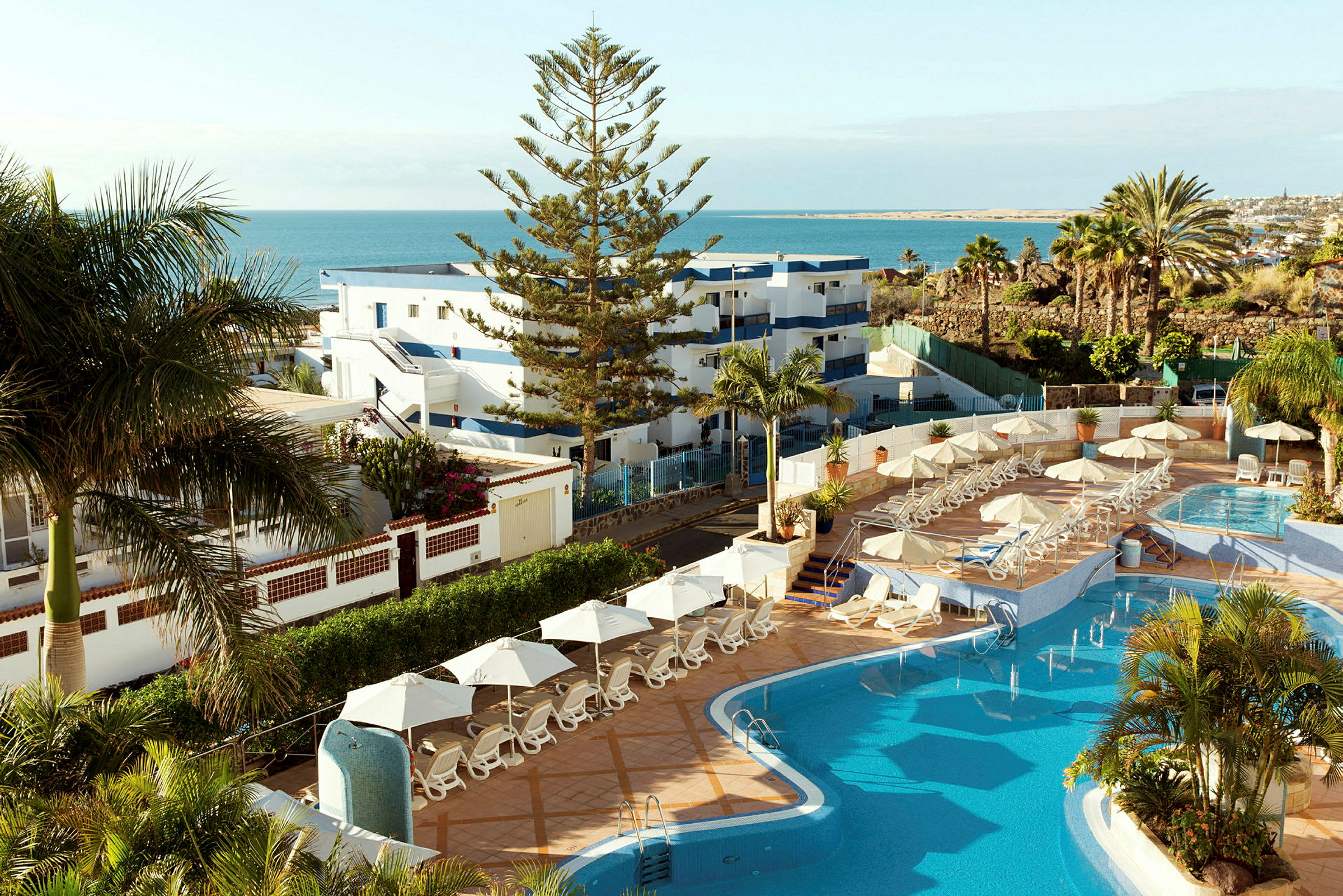 Bild på ett hotellområde med pool, solstolar och utsikt över havet. (AI-genererad text)