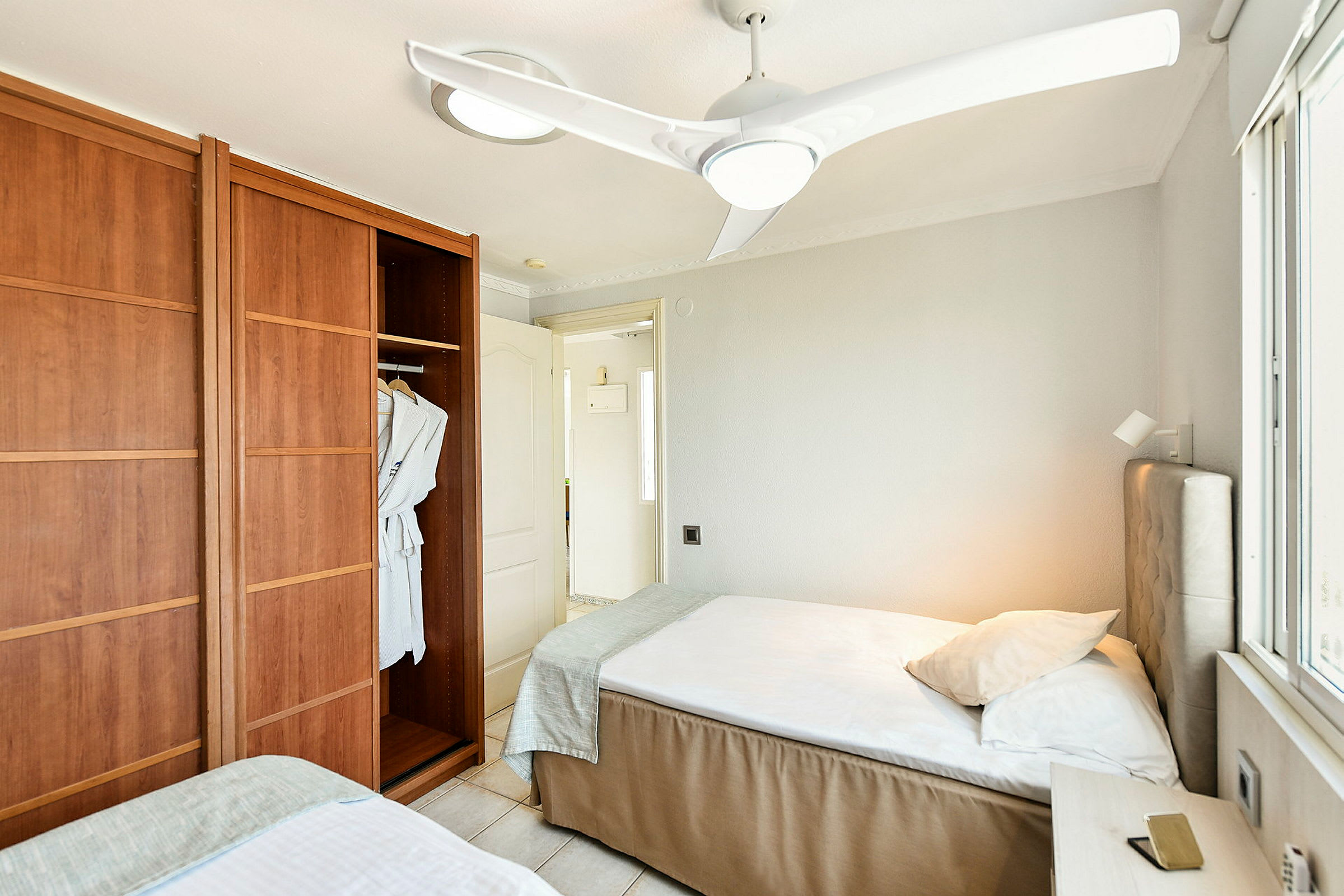Ett hotellrum med två enkelsängar, en garderob med badrockar och en takfläkt. (AI-genererad text)