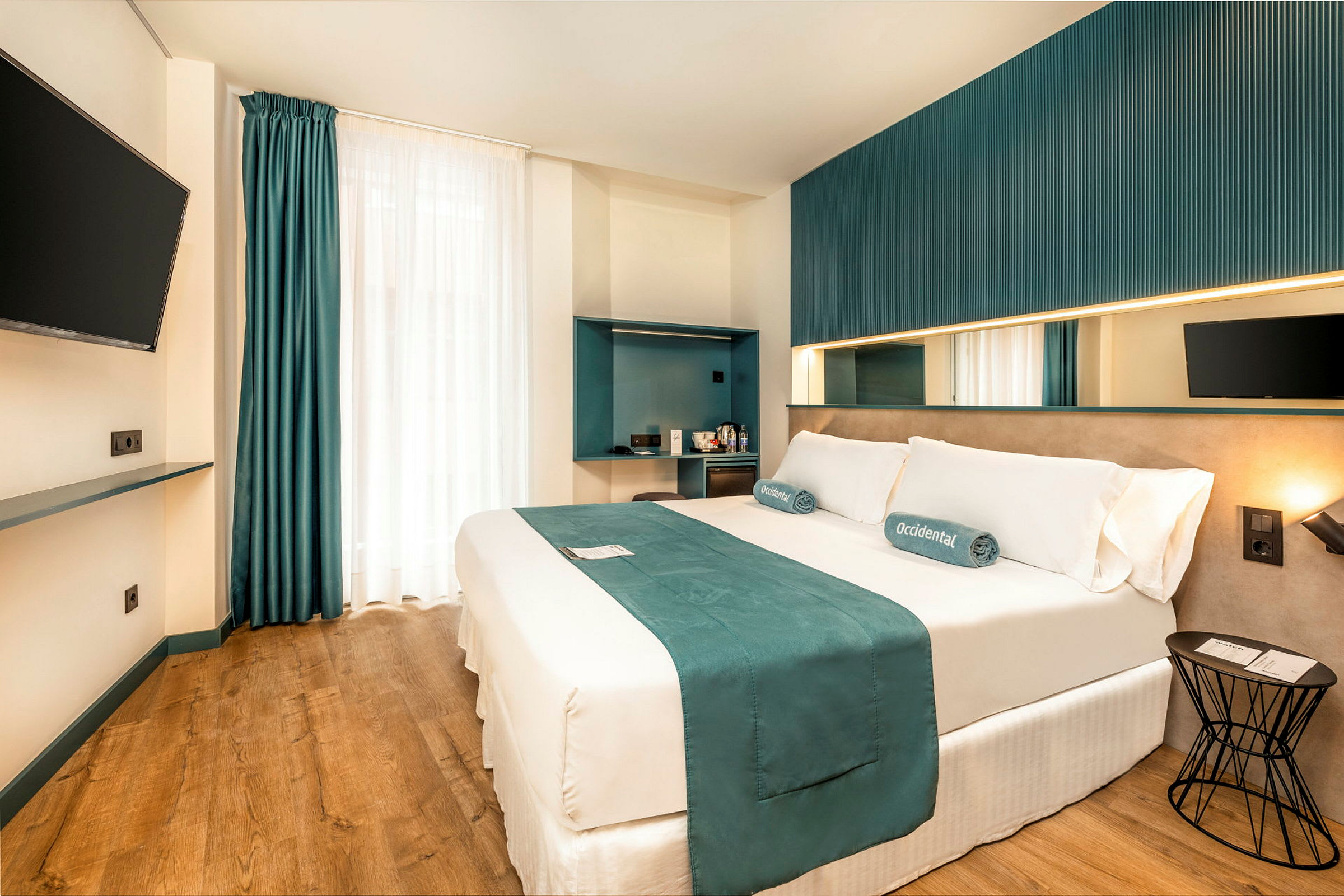 En modern hotellrum med en dubbelsäng, väggmonterad TV och minimalistisk inredning. (AI-genererad text)