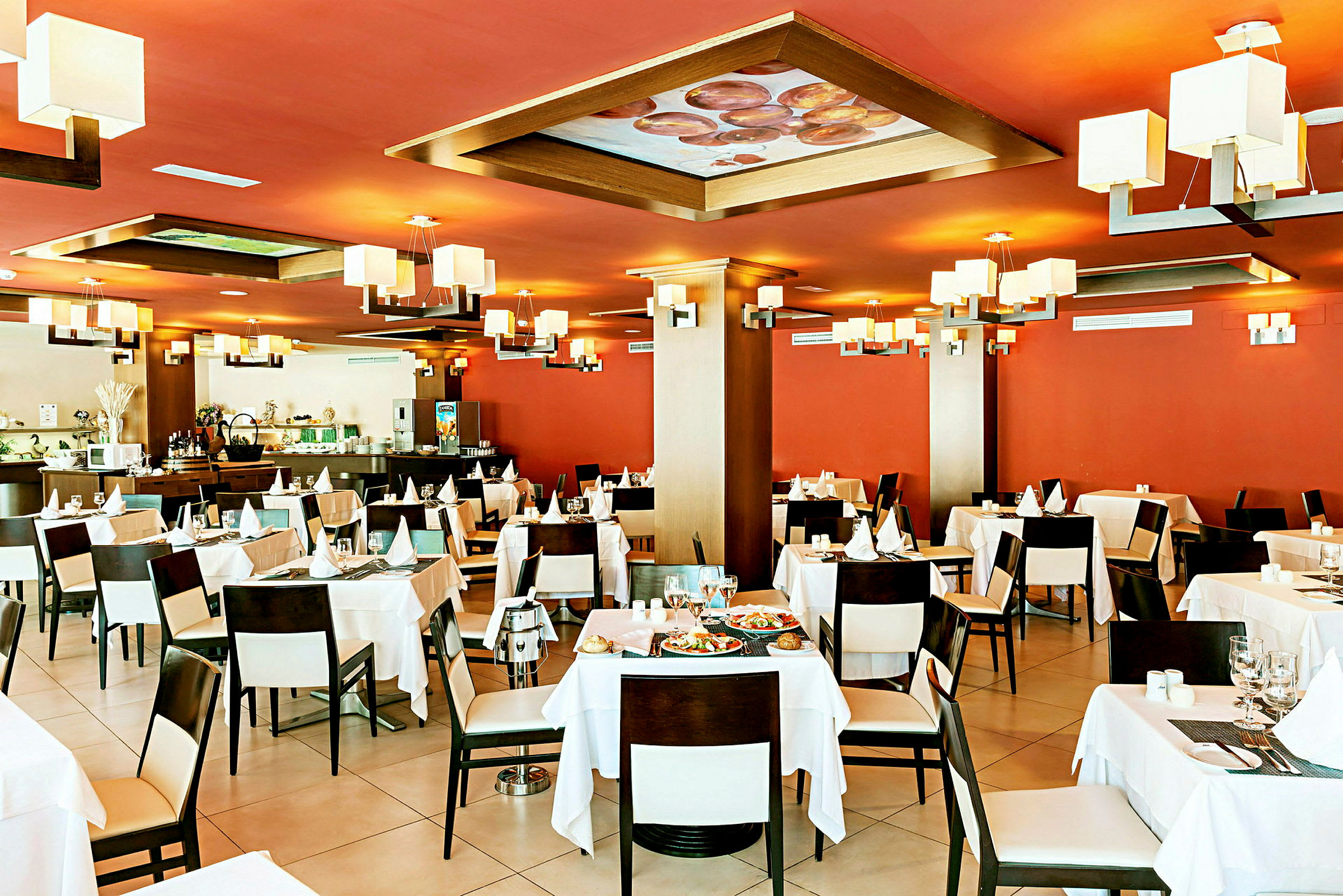 Interiör av en restaurang med röda väggar, vita dukar och modern belysning. (AI-genererad text)
