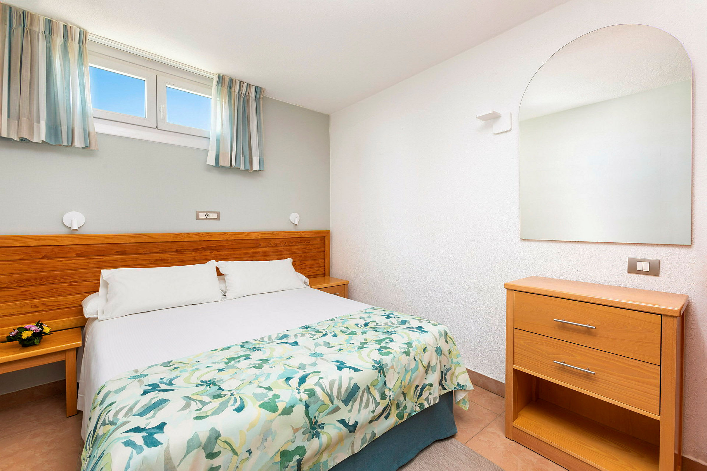 Ett hotellrum med en dubbelsäng, träpanel som sänggavel, och en spegel ovanför en byrå. (AI-genererad text)