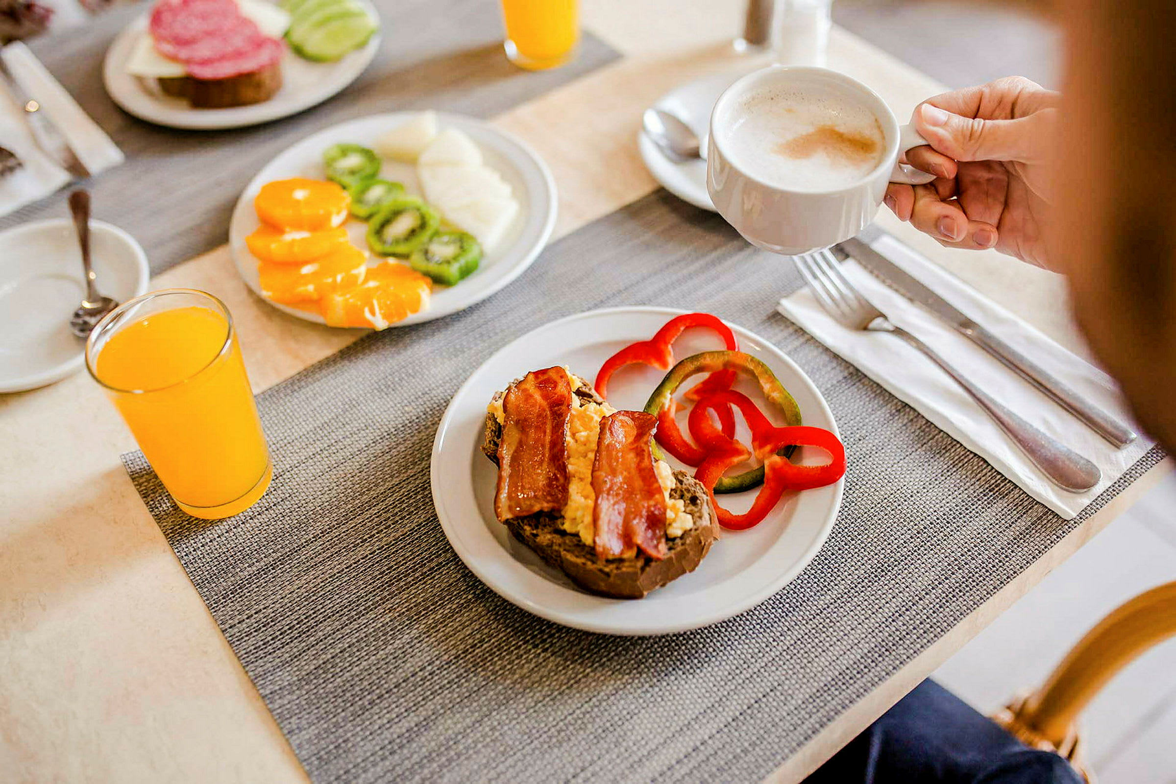 En upplagd frukost med macka, paprika, frukt, apelsinjuice och en kopp kaffe. (AI-genererad text)