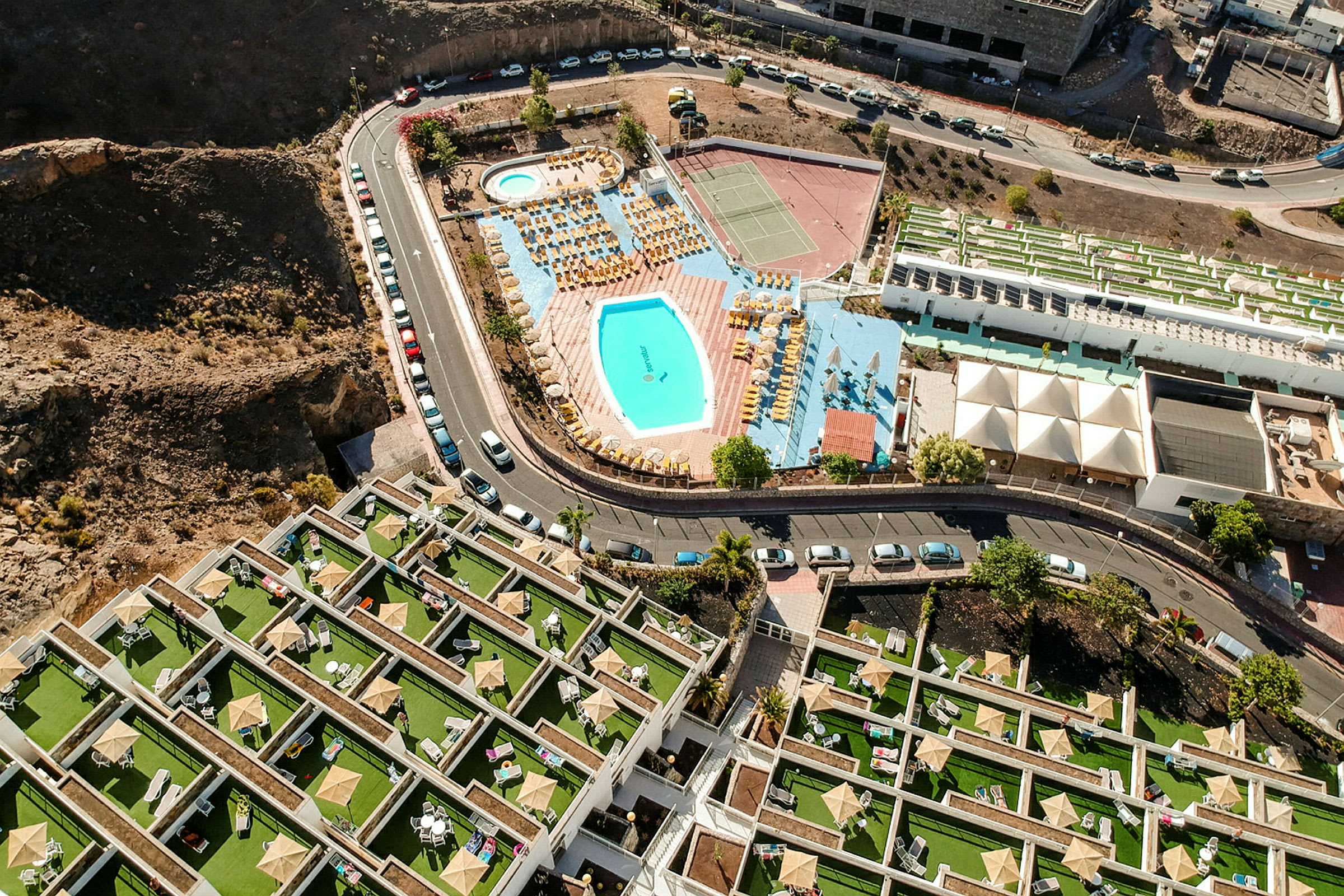 Flygbild av hotellområde med pool, solsängar och tennisbanor. (AI-genererad text)