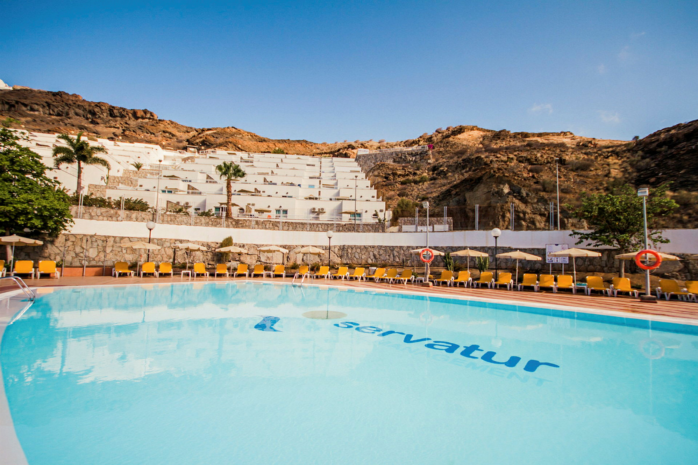 Utomhuspool vid ett semesterhotell med solstolar och utsikt över en sluttning med terrassbyggnader. (AI-genererad text)