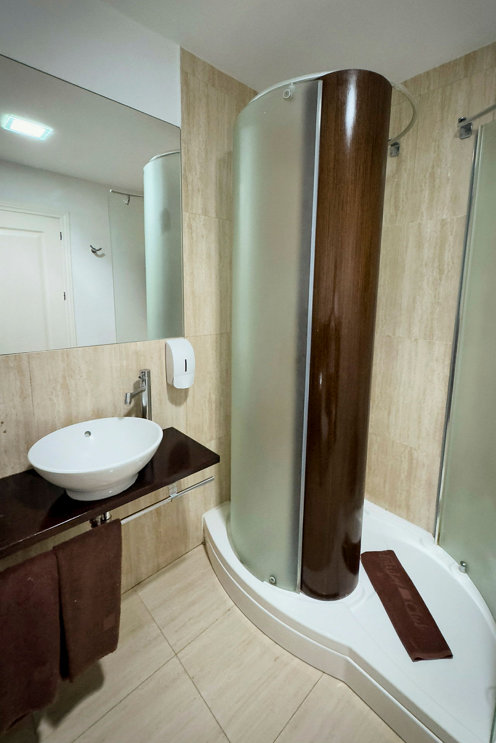 Badrum med en tvättställ, en brun handduk och en dusch med träpanel och frostat glas. (AI-genererad text)