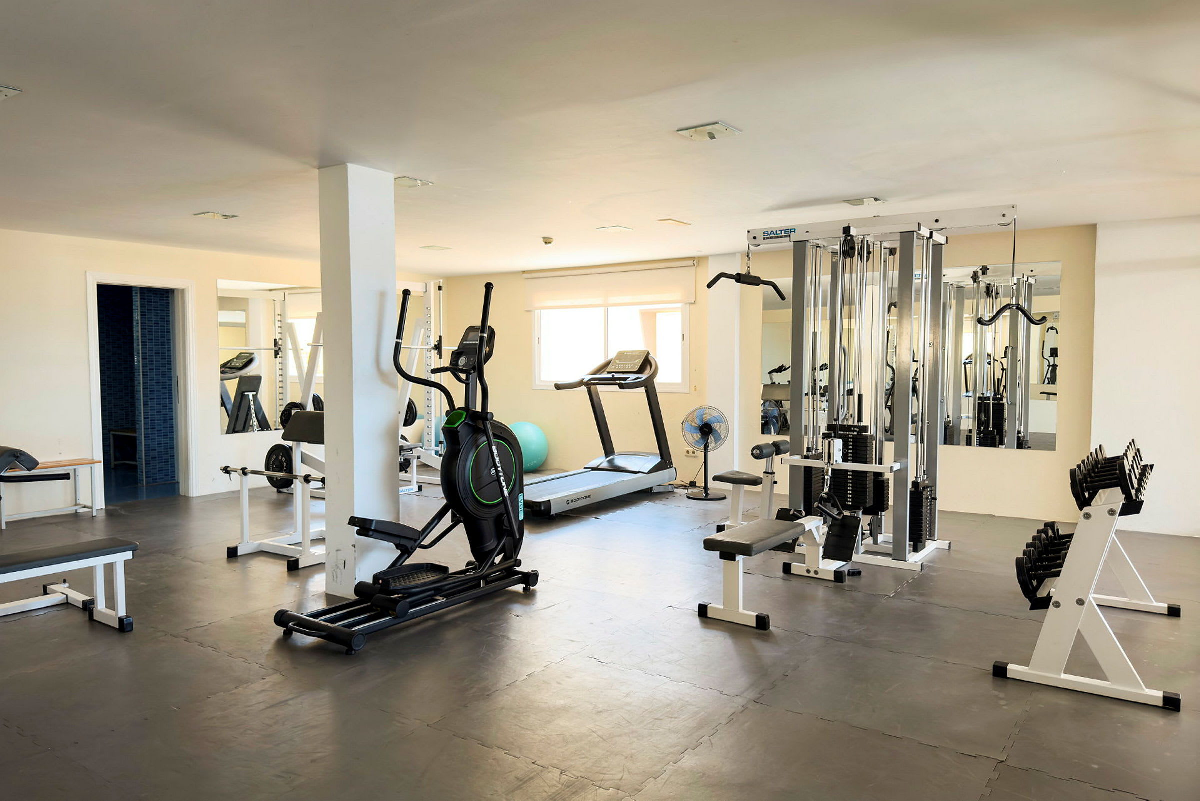 Ett gym med träningsutrustning som löpband, elliptisk träningsmaskin, styrketräningsmaskiner och hantlar. (AI-genererad text)