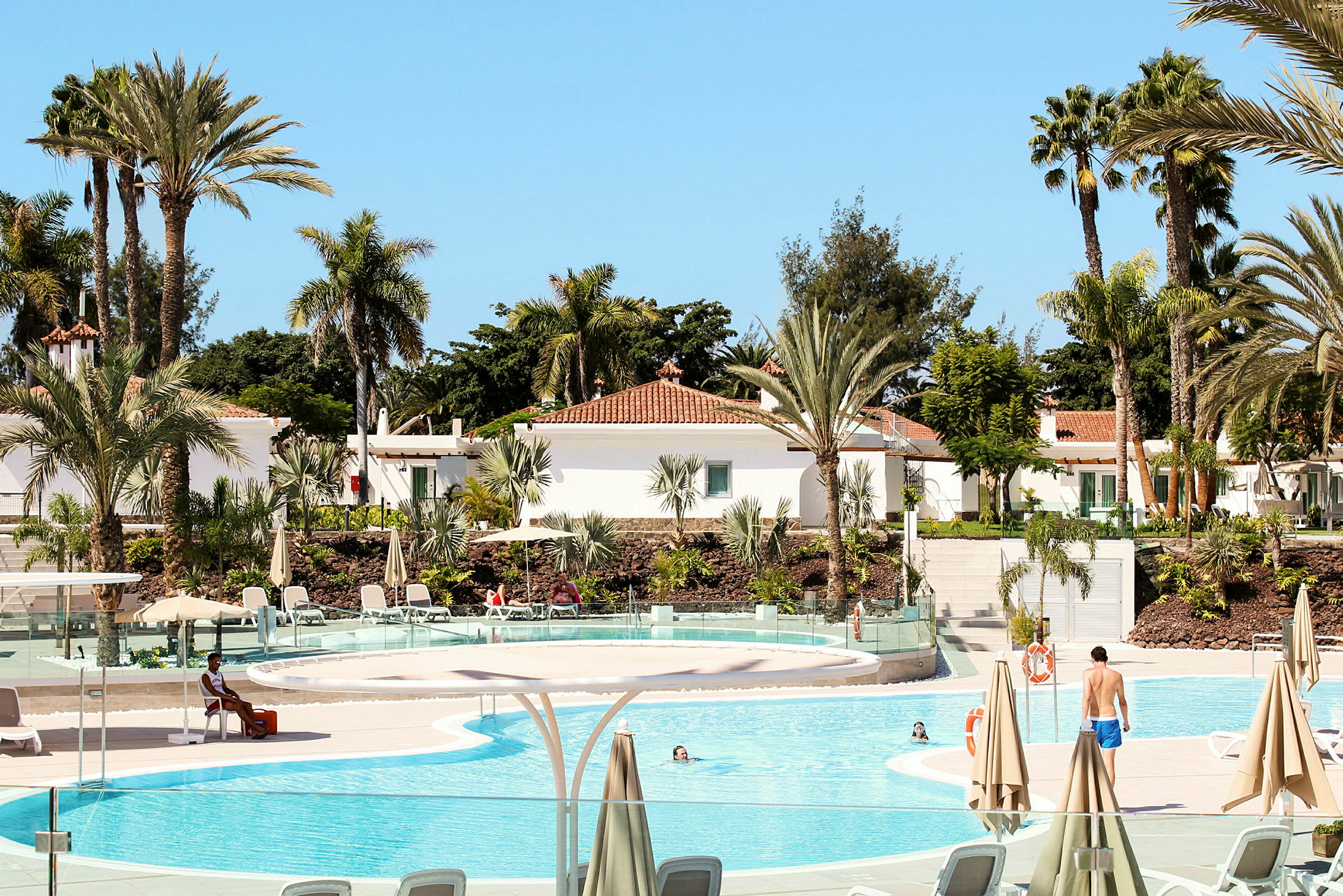 En solig resort med pool, palmer och vita byggnader. (AI-genererad text)