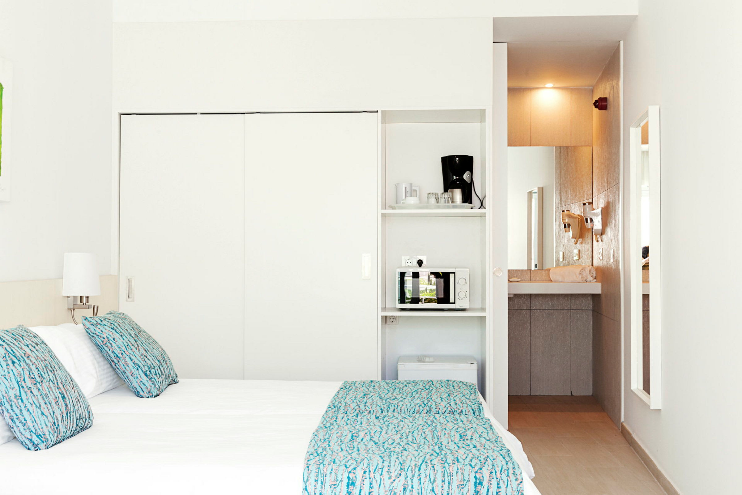 Ett hotellrum med en säng, lampor, och ett minikök som inkluderar en mikrovågsugn och en kaffemaskin. (AI-genererad text)