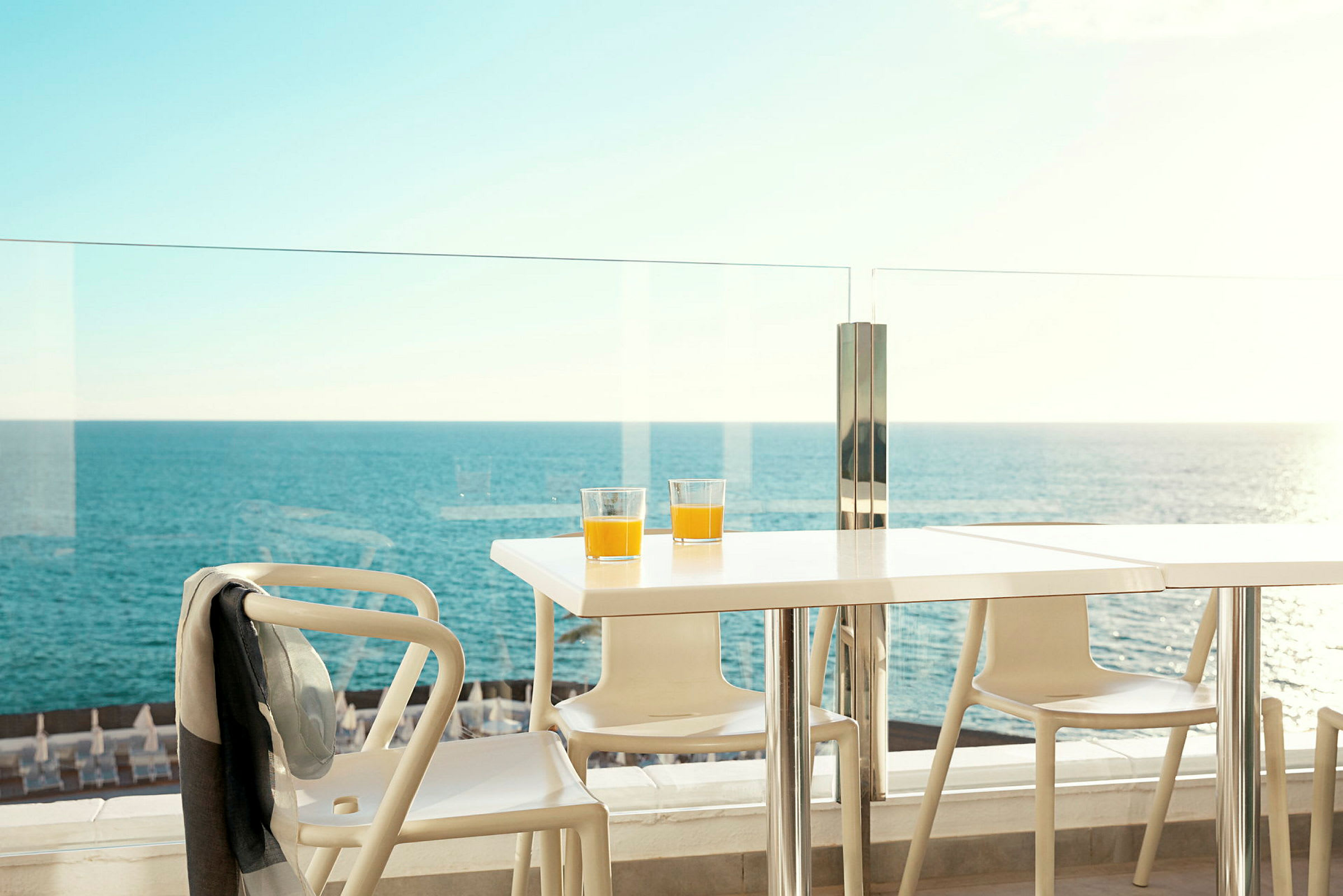 Bord med två glas apelsinjuice på en terrass med utsikt över havet. (AI-genererad text)