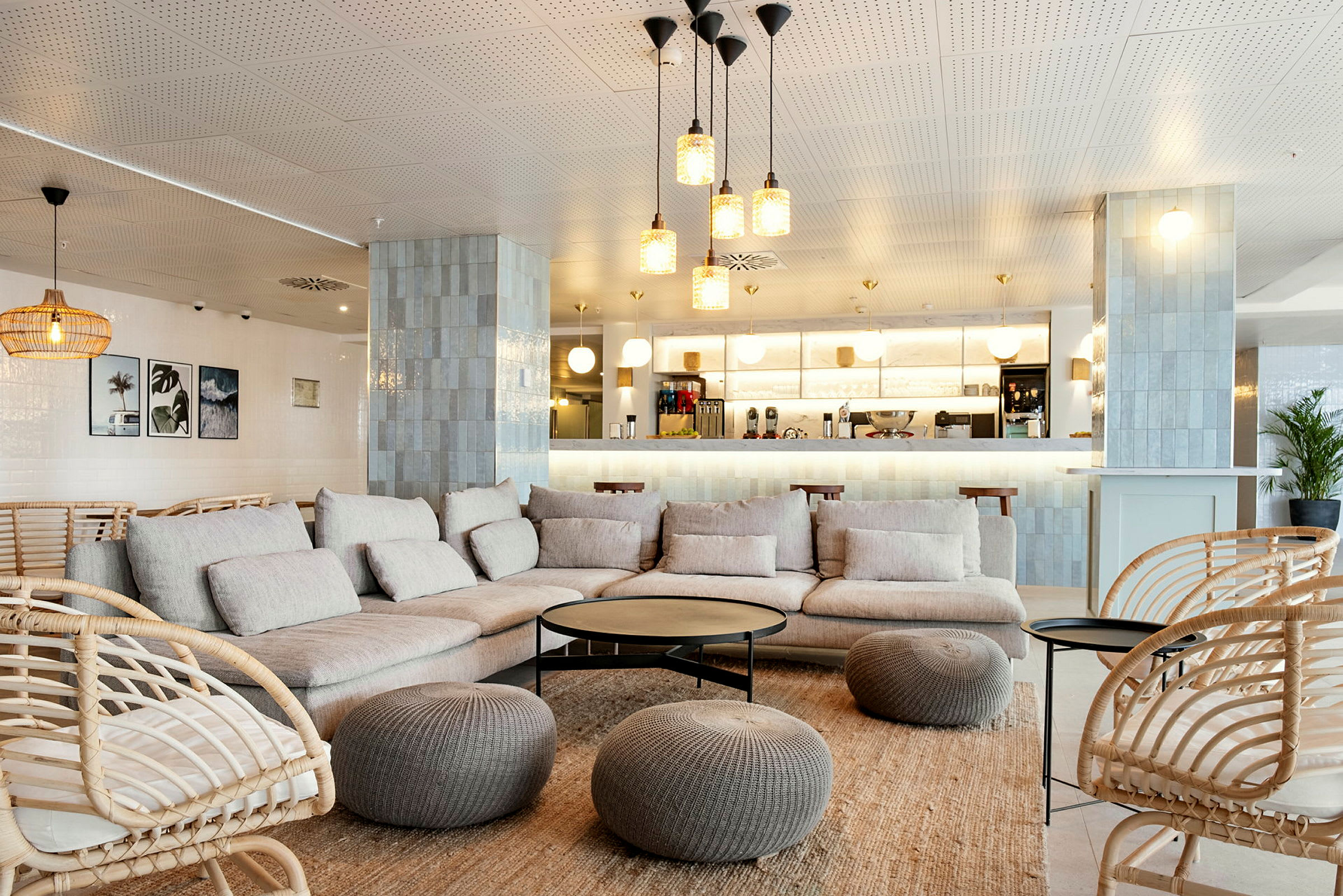 En modern lounge med beige soffor och korgstolar, inredd med bord och dekorationer samt en kaffebar i bakgrunden. (AI-genererad text)