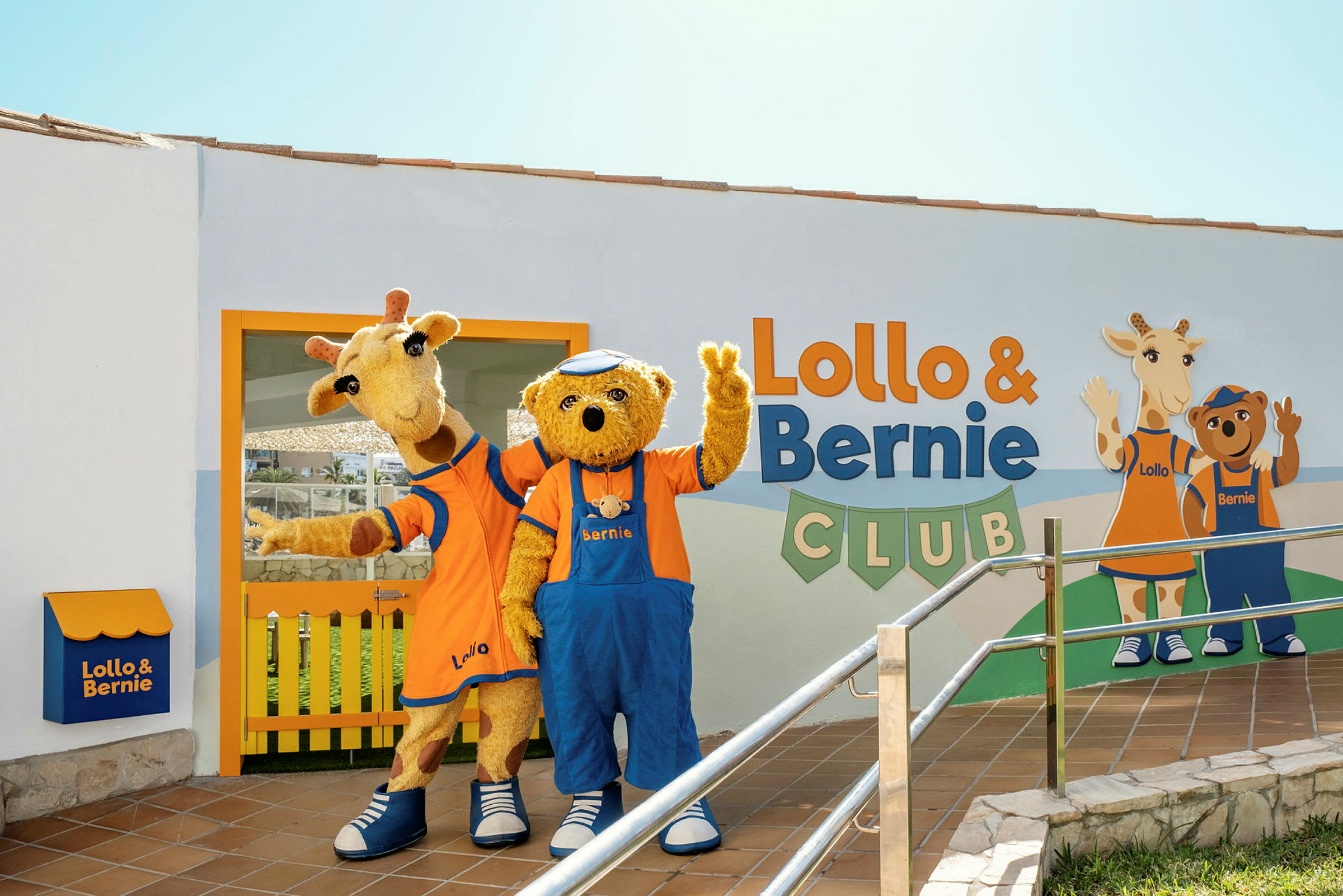 Två maskotar, en giraff och en björn, står framför byggnaden för Lollo & Bernie Club och vinkar. (AI-genererad text)