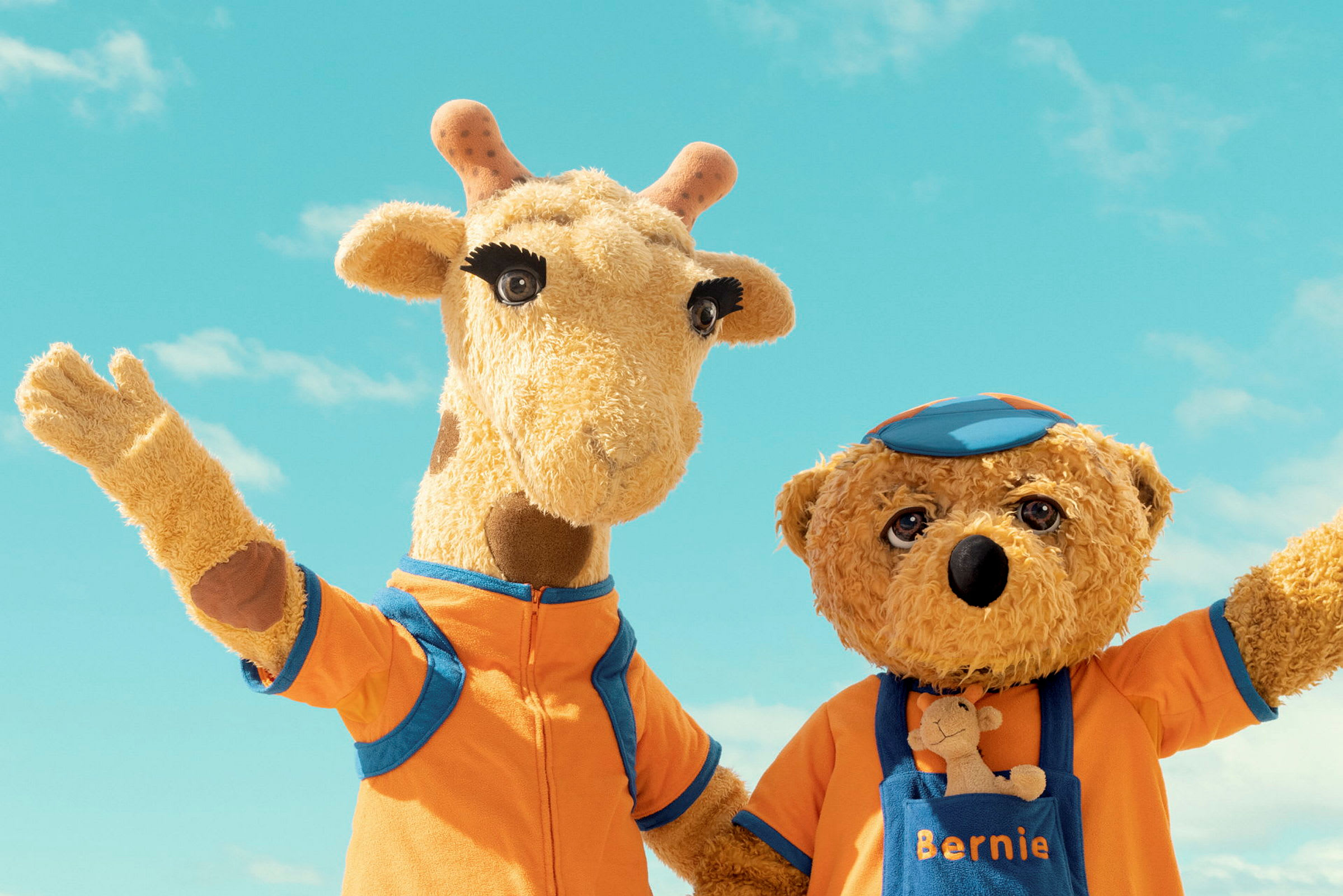 Två mjukisdjur, en giraff och en björn, poserar tillsammans framför en blå himmel. (AI-genererad text)