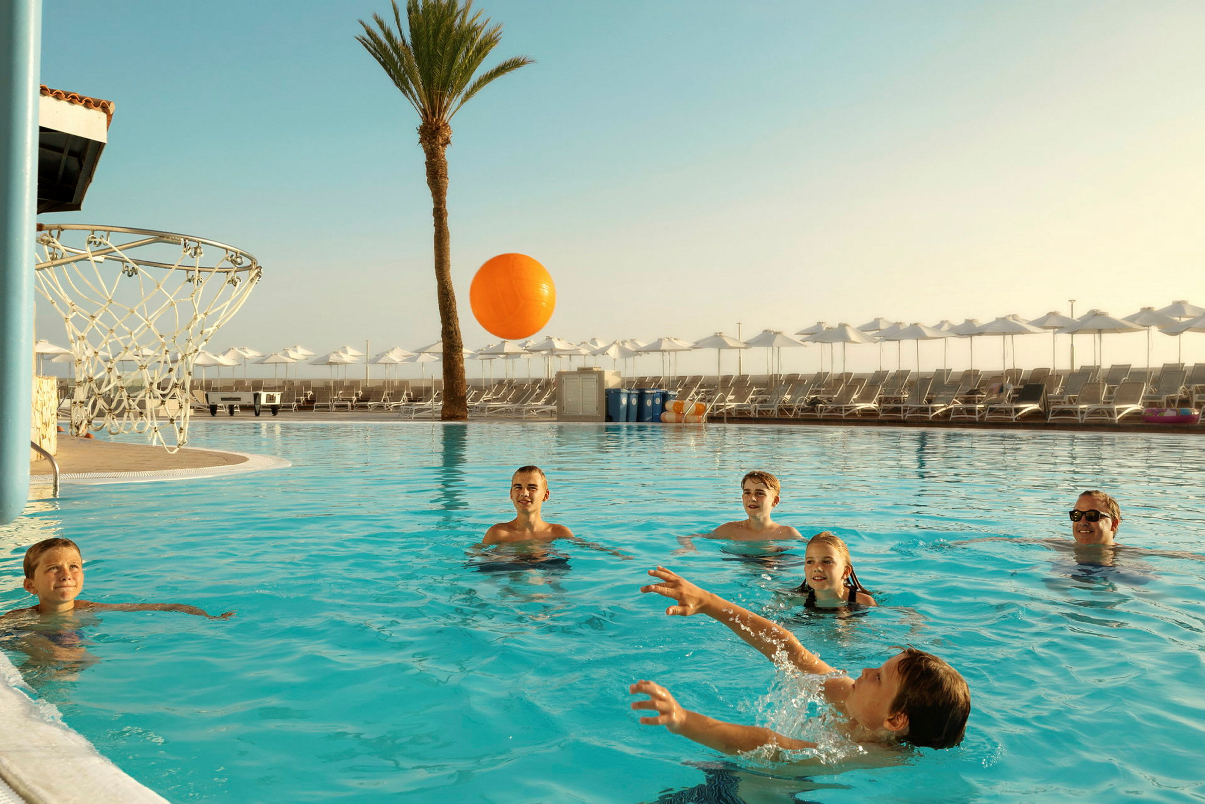 Pool med en basketkorg och personer som spelar med en orange boll. (AI-genererad text)