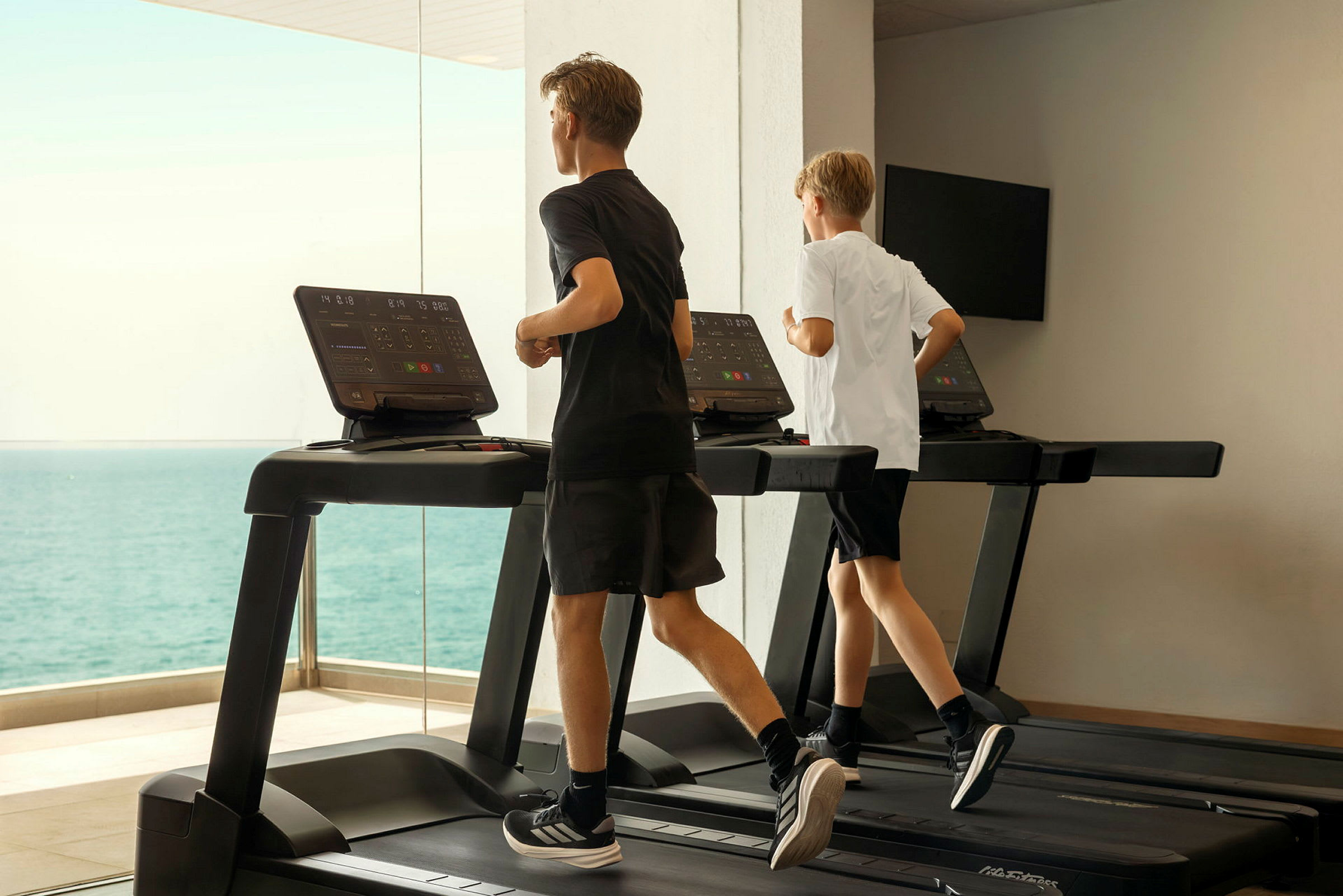 Två personer springer på löpband vid ett gym med havsutsikt. (AI-genererad text)