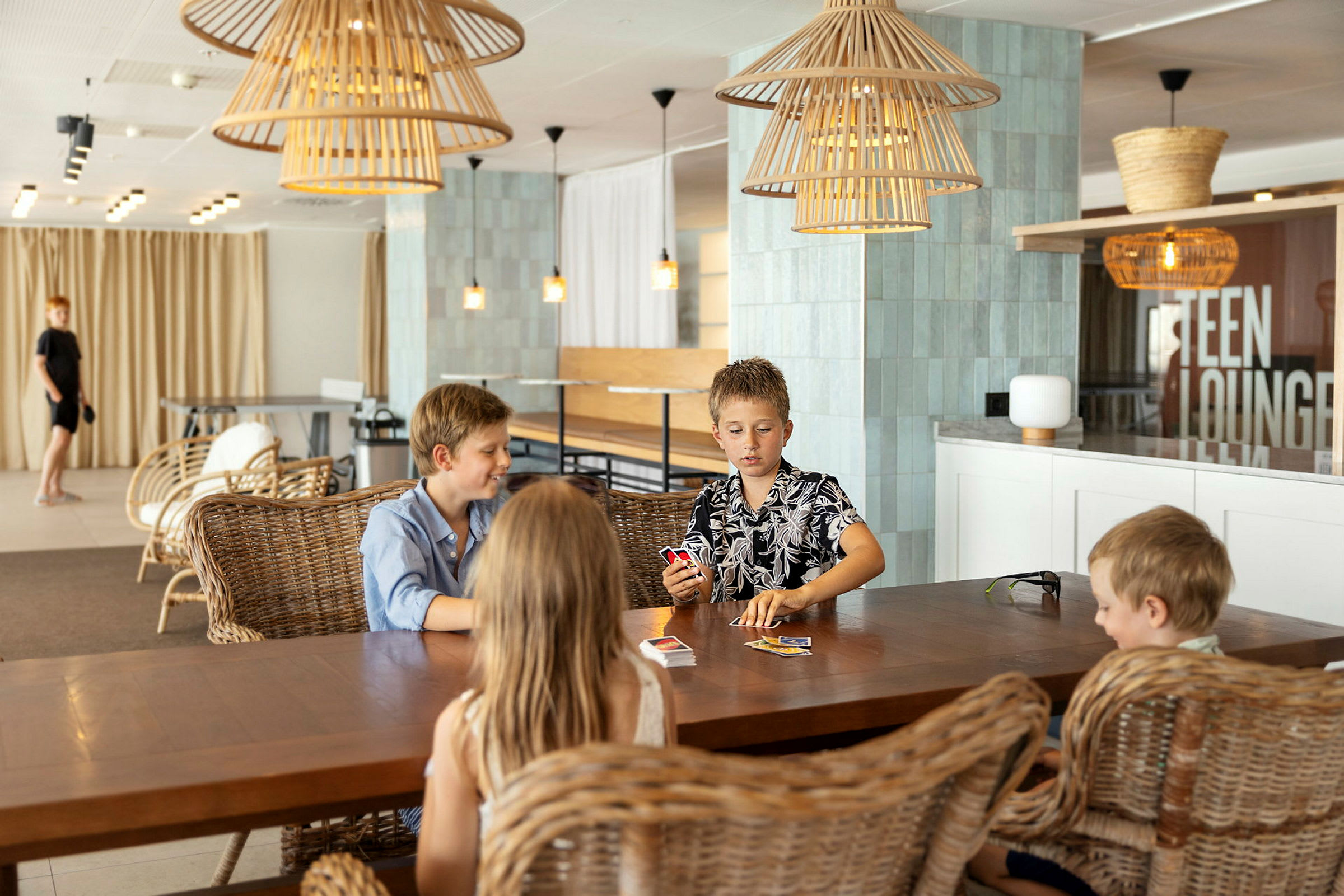 Fyra personer sitter vid ett bord och spelar kort i en modern lounge. (AI-genererad text)