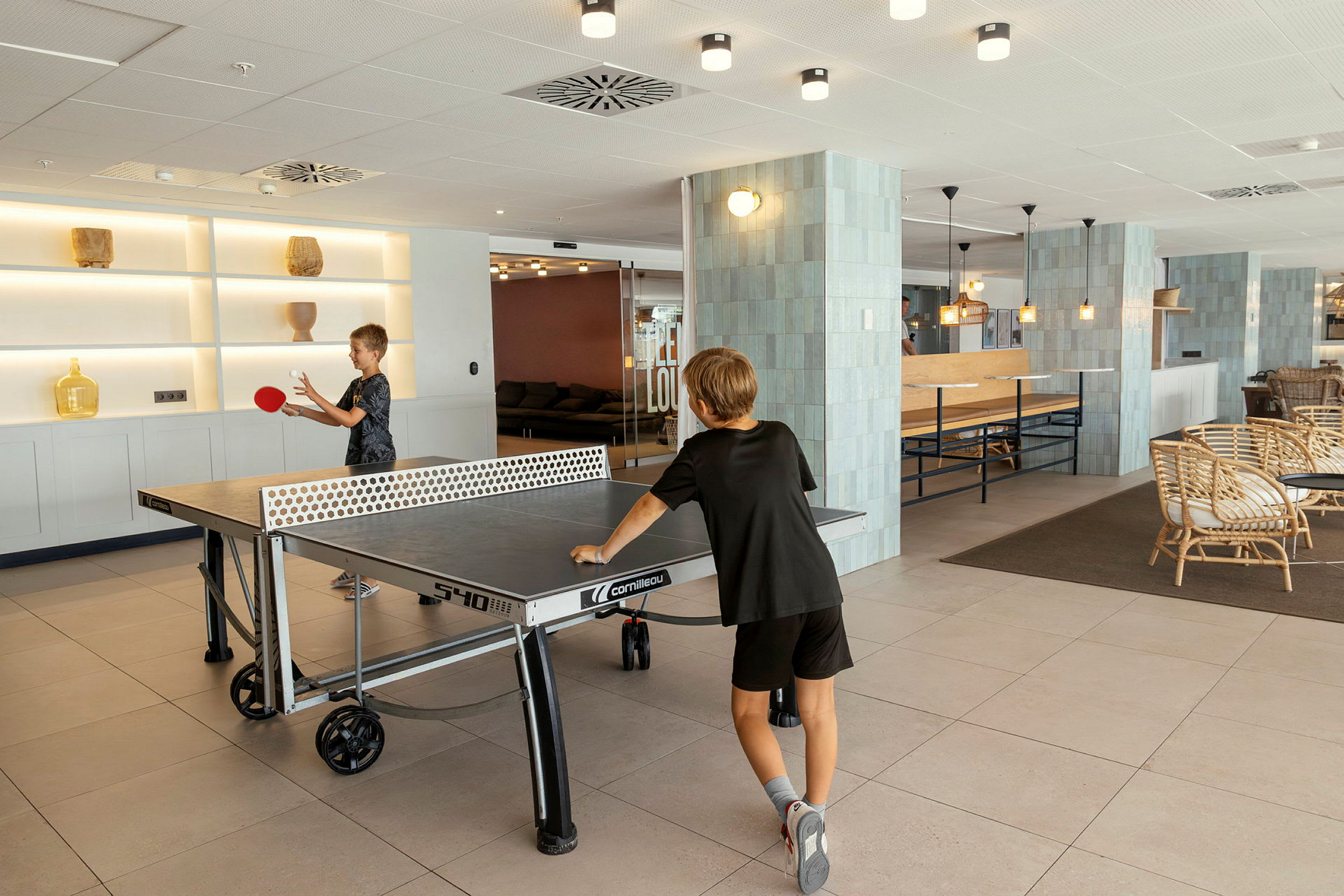Två personer spelar bordtennis i en ljust inredd gemensamhetslokal. (AI-genererad text)