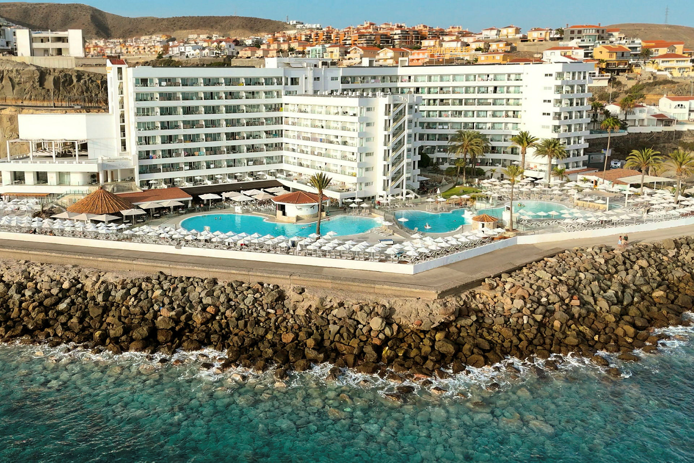 Hotell vid kusten med flera pooler och solstolar. (AI-genererad text)