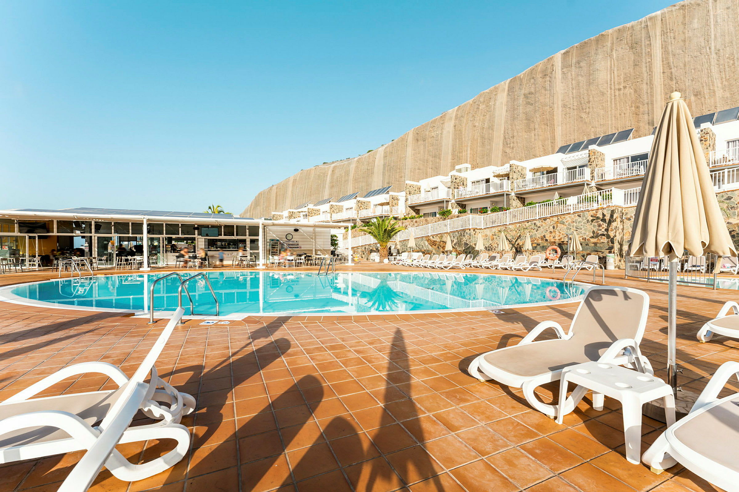 Utomhuspool med solstolar och parasoller vid en hotellbyggnad. (AI-genererad text)