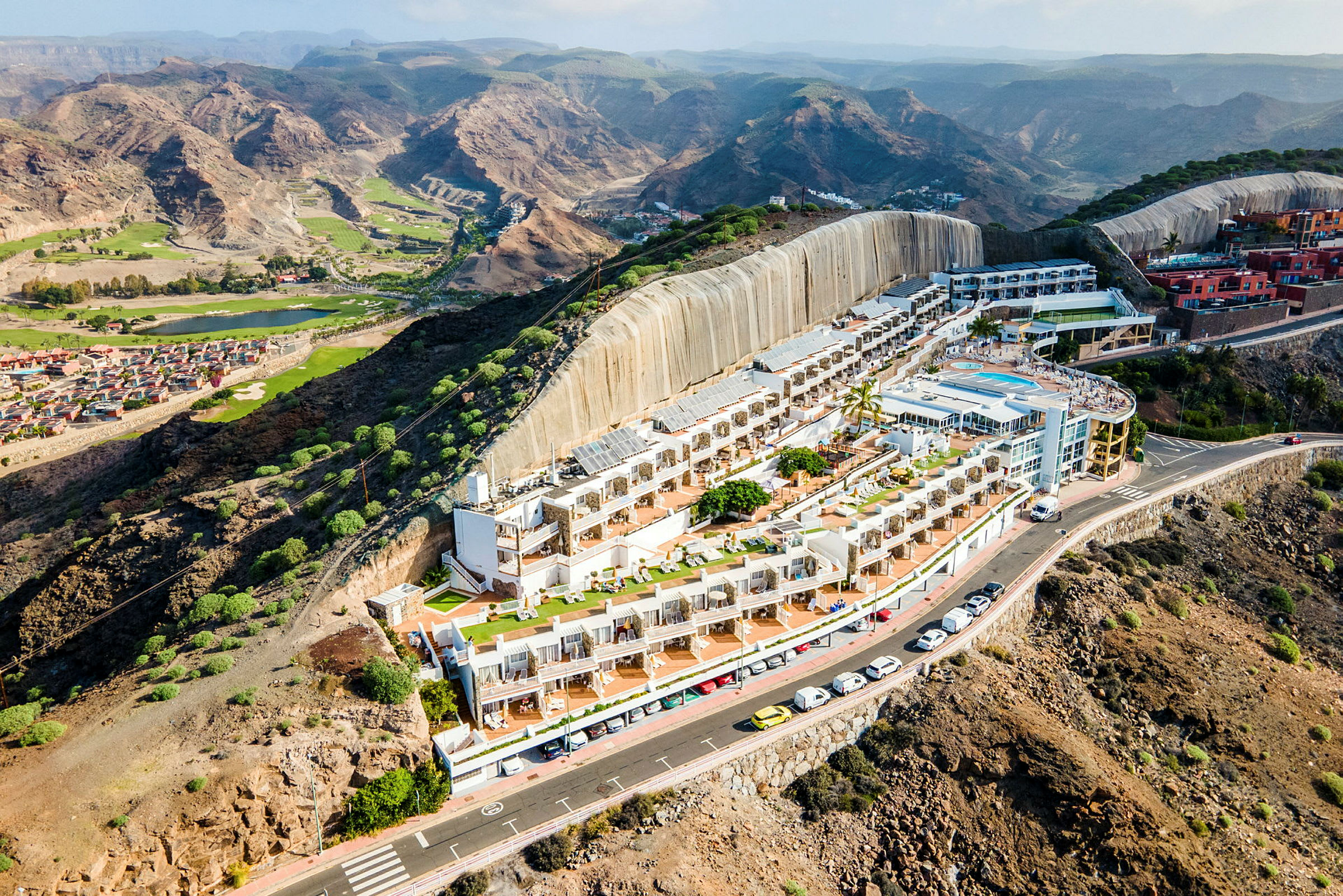 Hotellkomplex med poolområde beläget på en bergssluttning, omgiven av naturlandskap och dalar. (AI-genererad text)