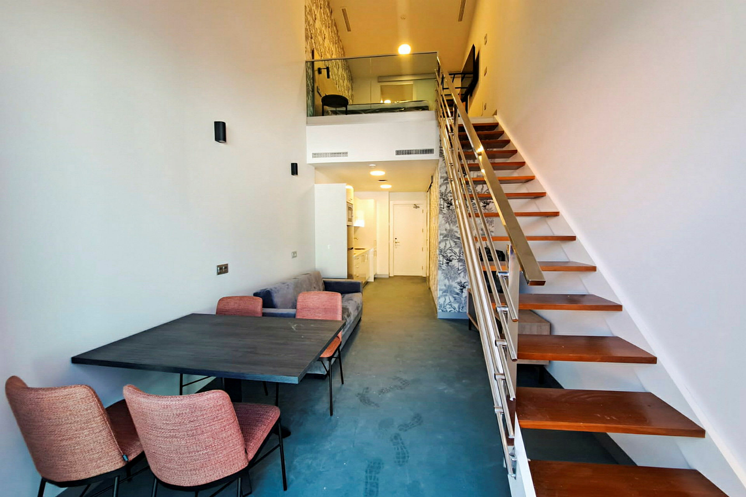 Bild av ett modernt loft med en trappa, ett matbord och stolar, samt en mindre kökspentry och soffa. (AI-genererad text)