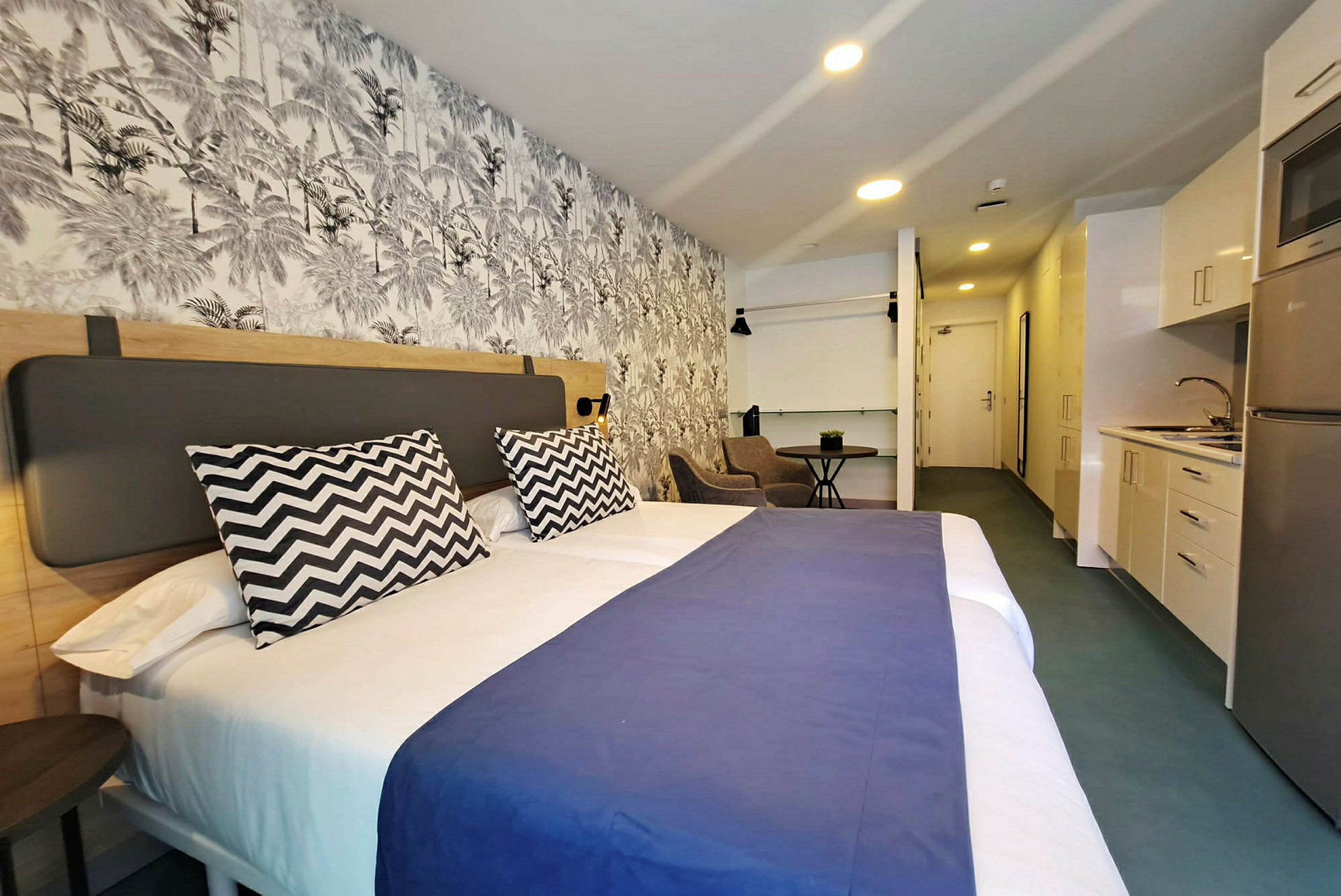 Hotellrum med en stor säng, dekorativ vägg och ett mindre kök. (AI-genererad text)