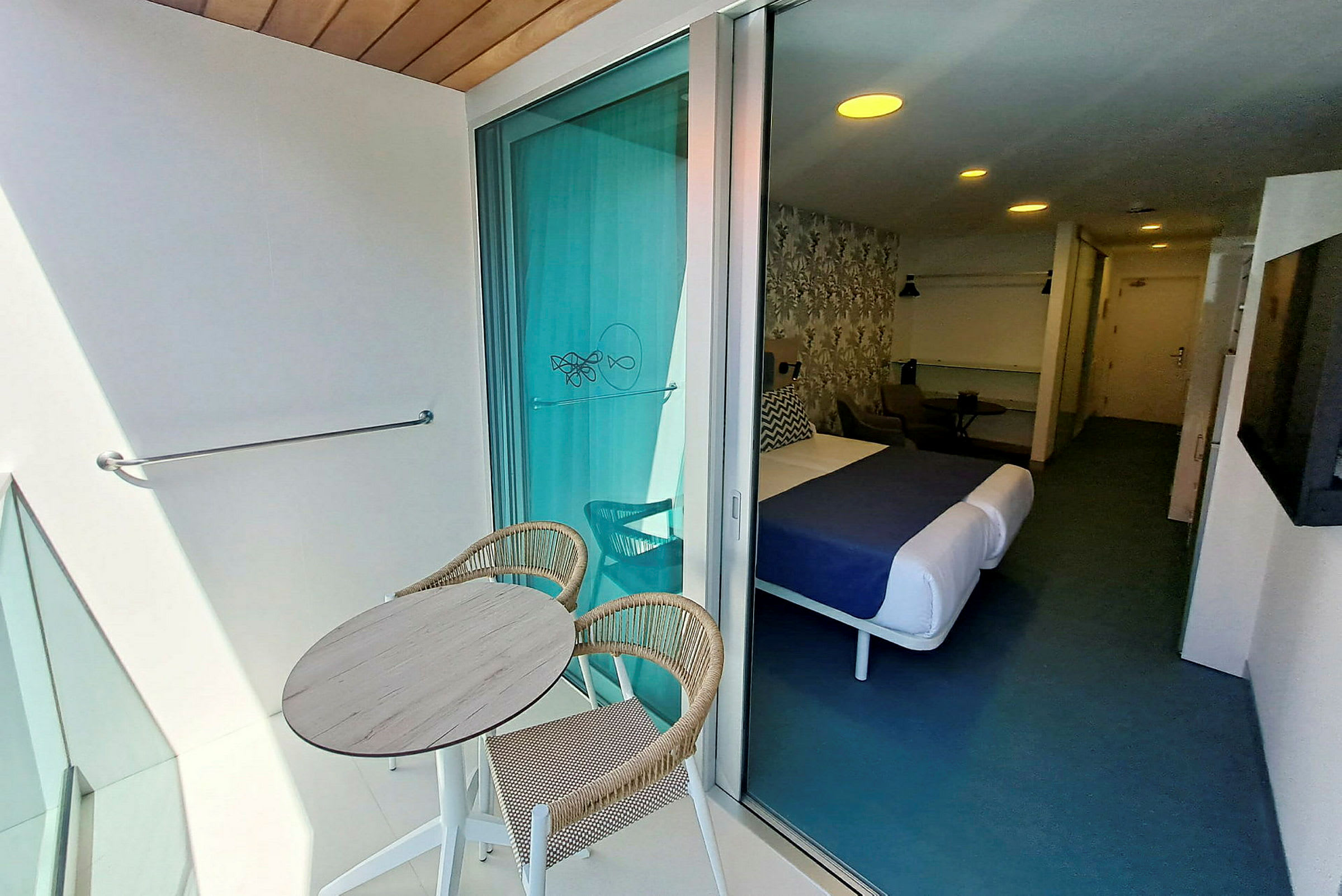 Bild på ett hotellrum med en balkong. På balkongen finns ett runt bord med två stolar. (AI-genererad text)